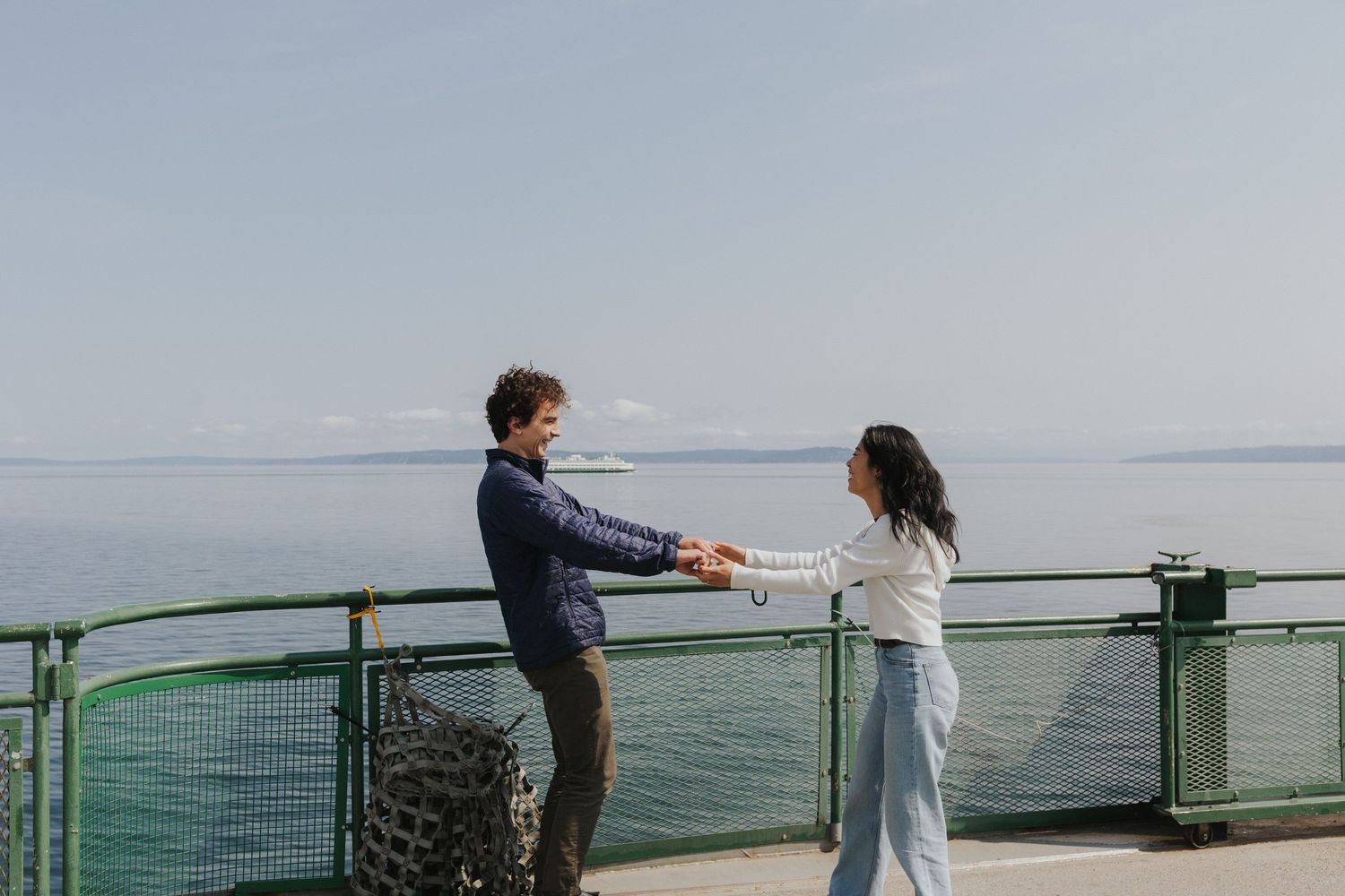 Couple standing at a ferry railing overlooking the ocean on a bright day.