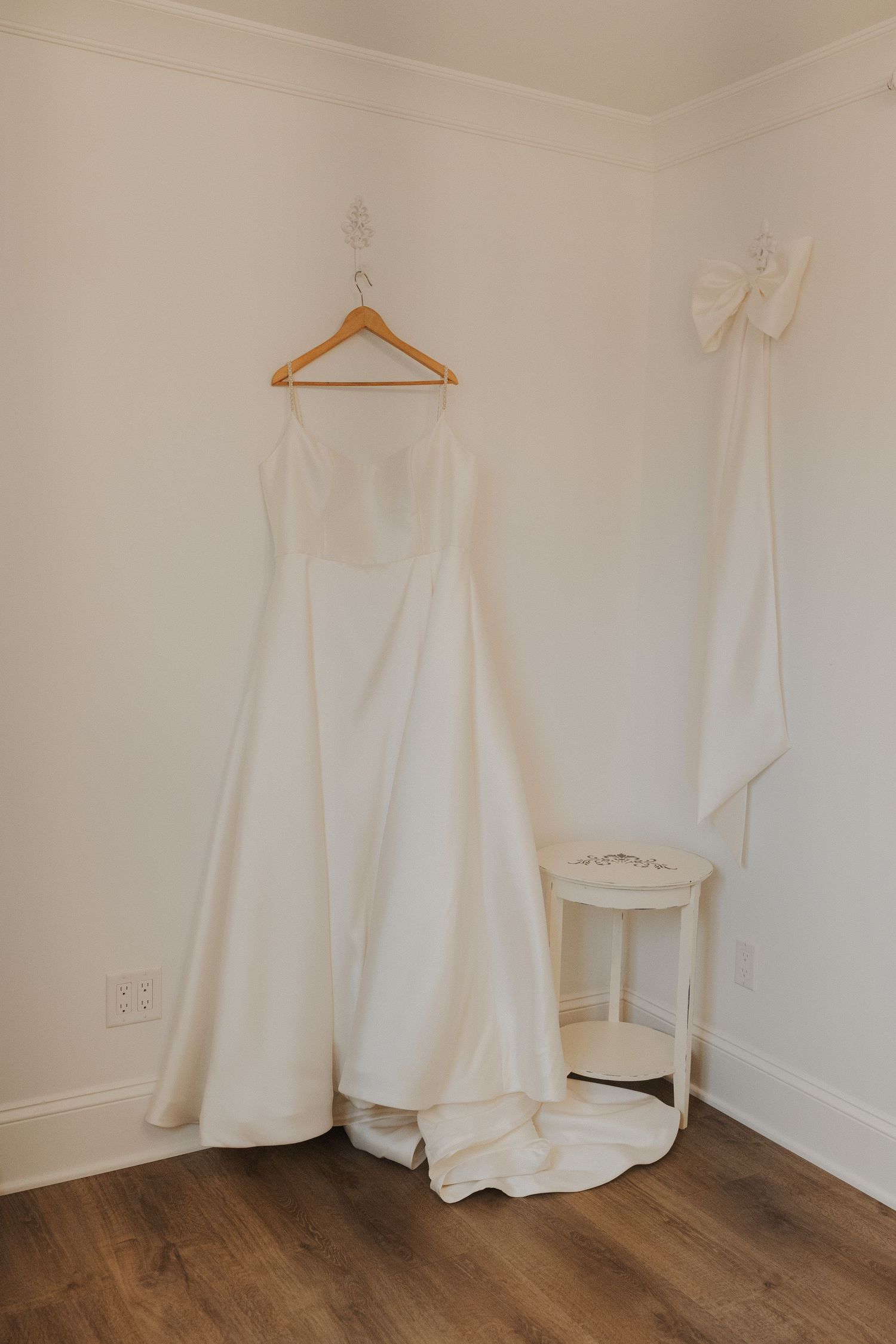 Wedding dress collection displayed on hangers against white walls with wooden flooring.