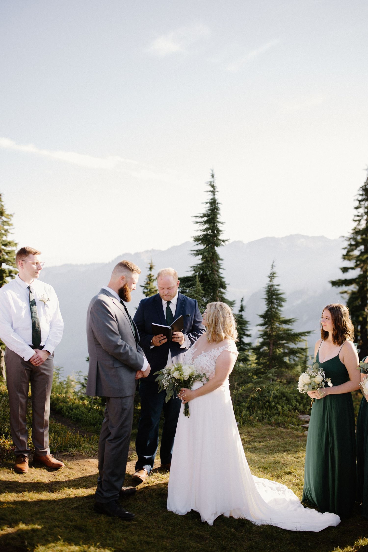 Wedding ceremony guests gather on a mountainside as vows are exchanged under blue skies.