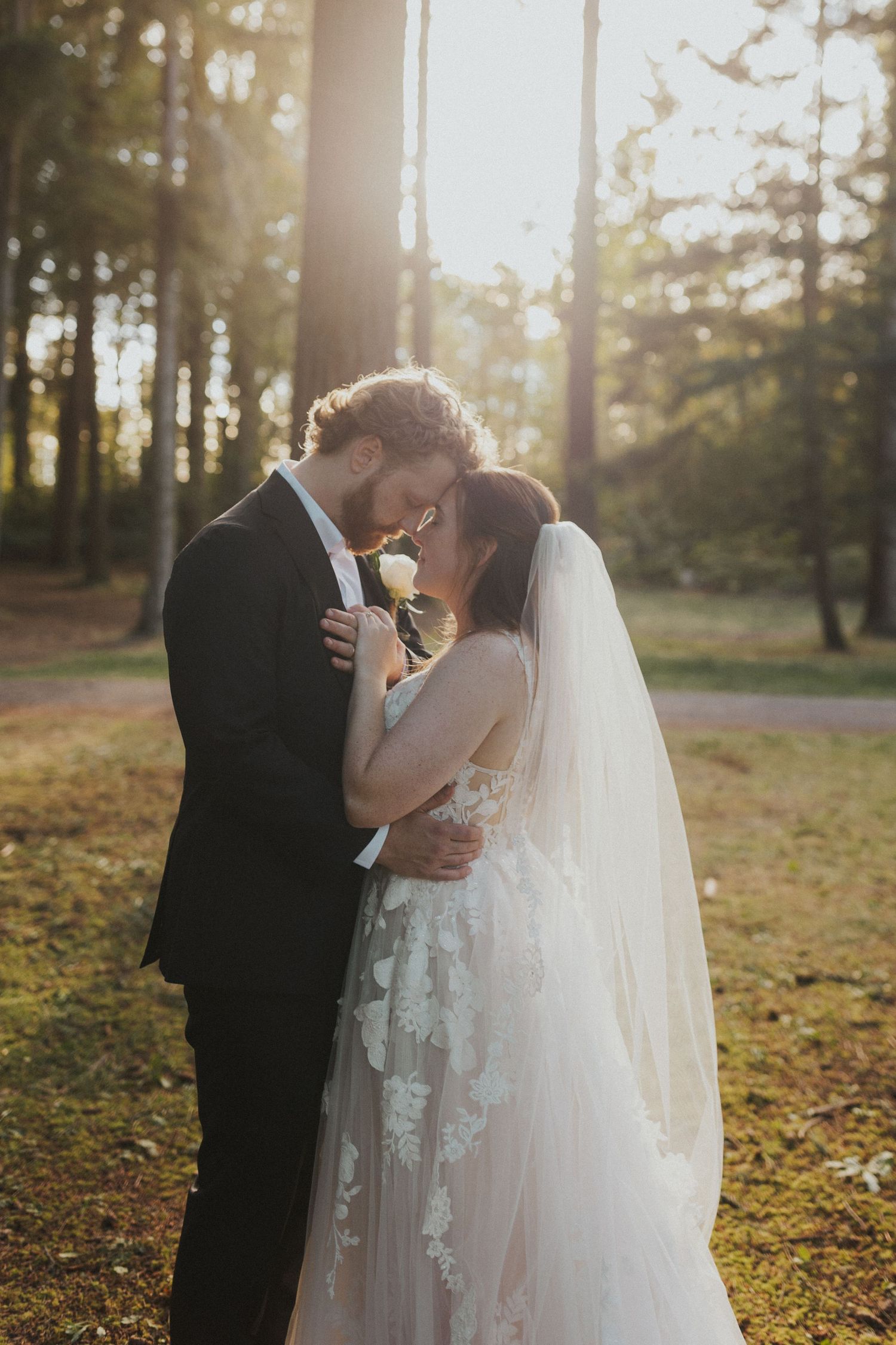 Intimate wedding moment captured in a sunlit forest with a couple sharing a tender embrace.