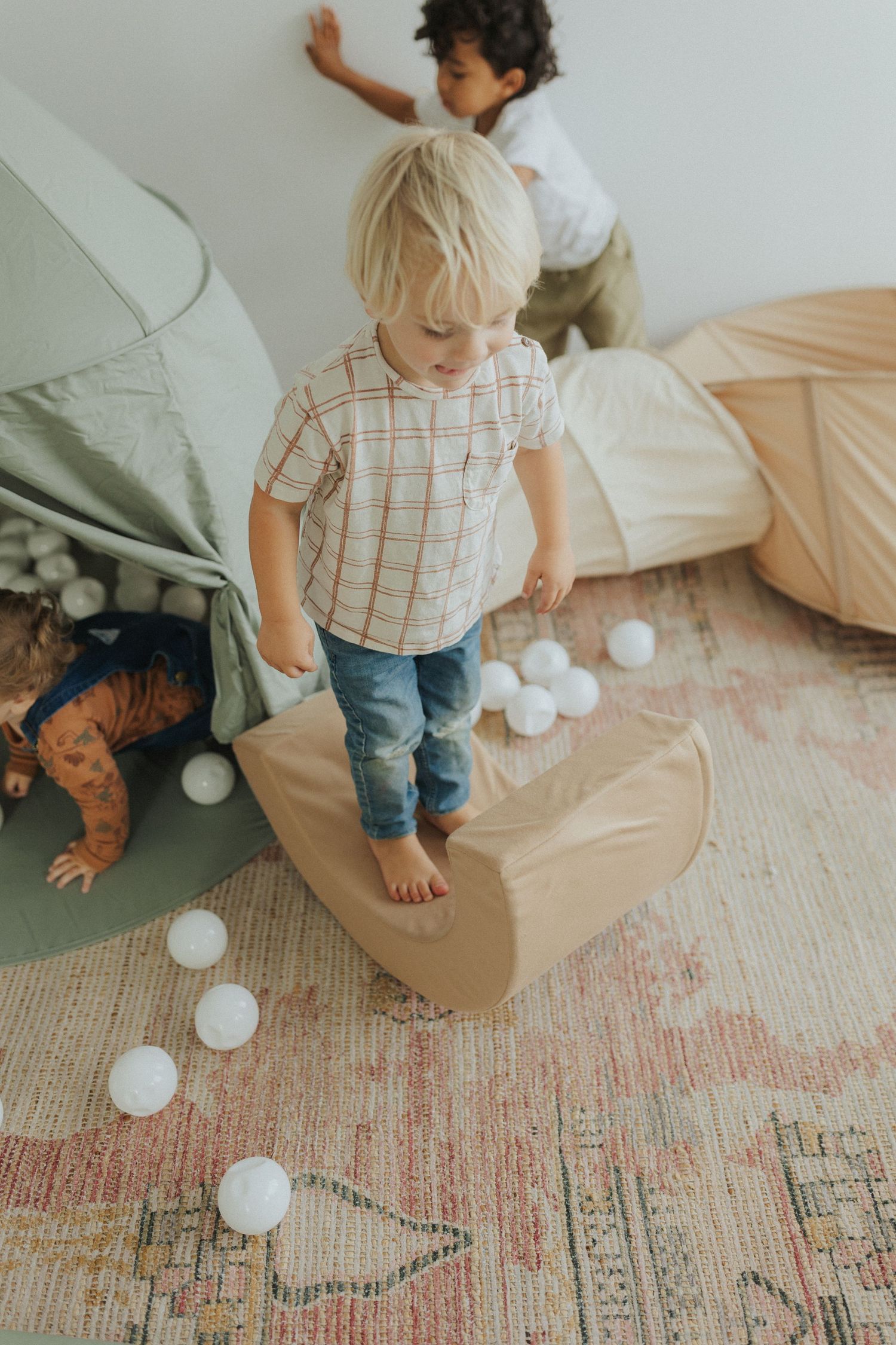 Small child playing with white balloons on a patterned area rug in a minimalist room setting.