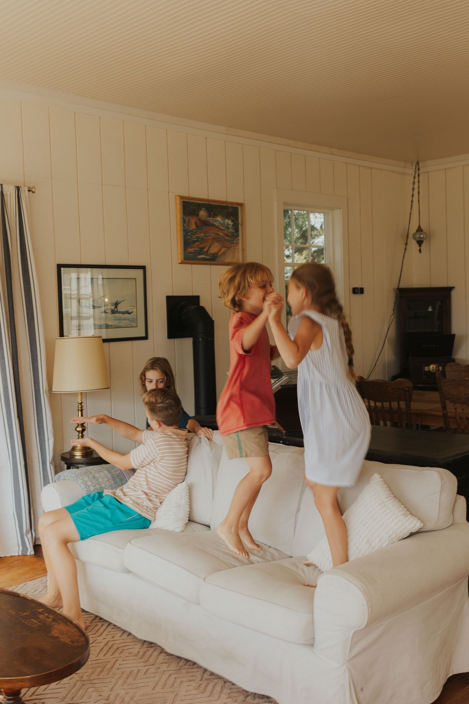 Playful group jumping on a large white couch in a bright living room.