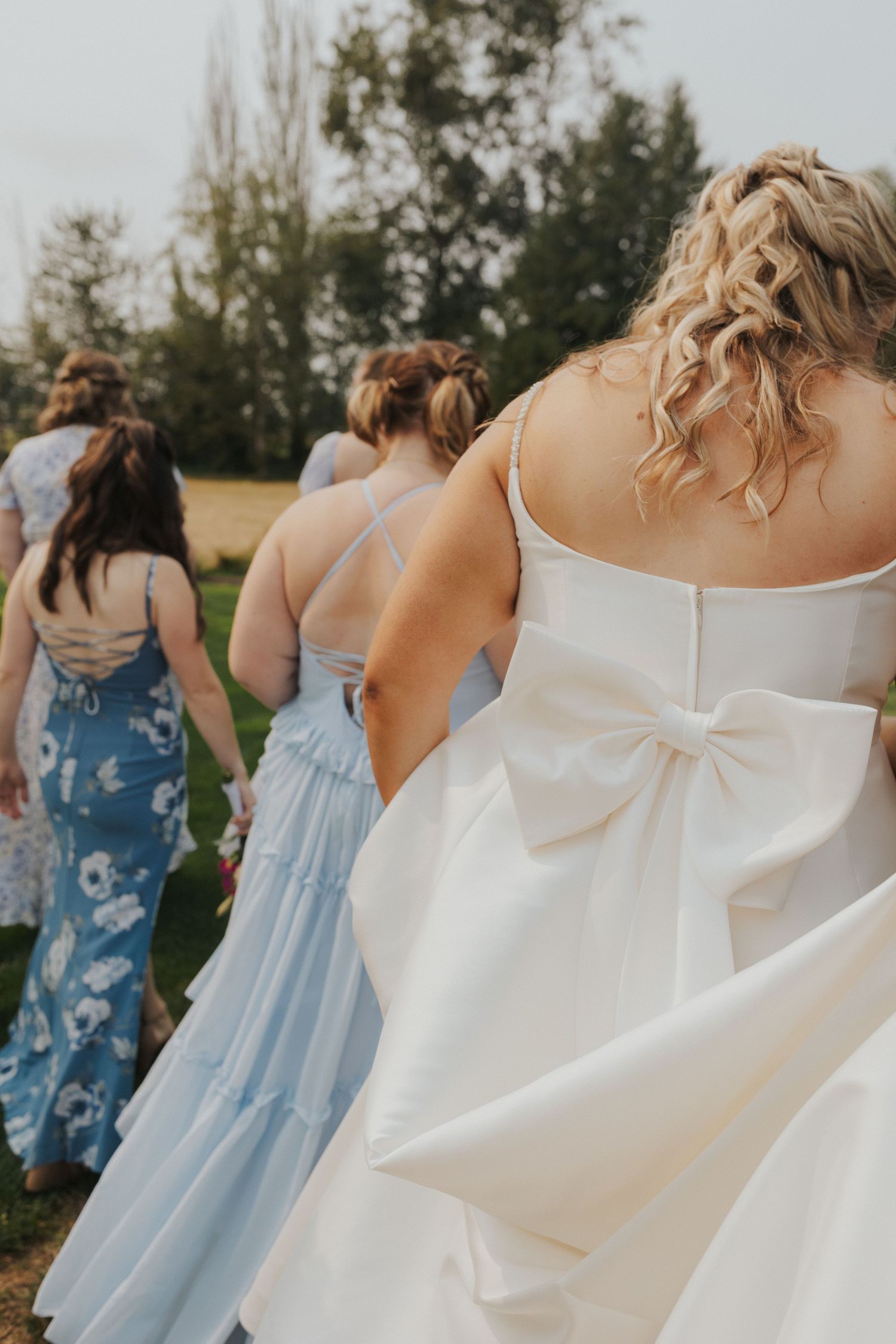 Wedding party members in blue dresses and white gown walk together against a natural backdrop.