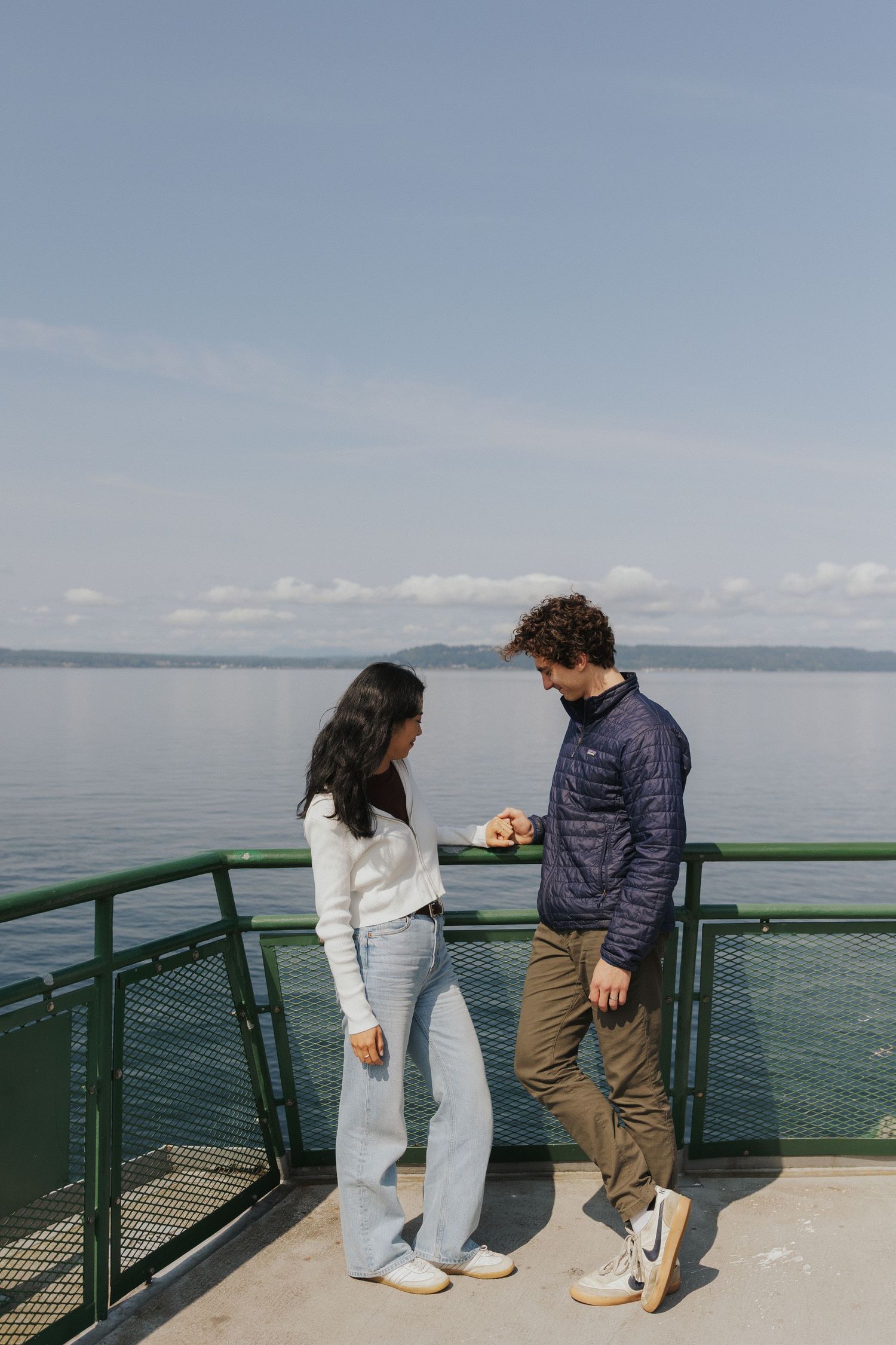 Two people stand together on an observation deck with blue water and sky in the background.