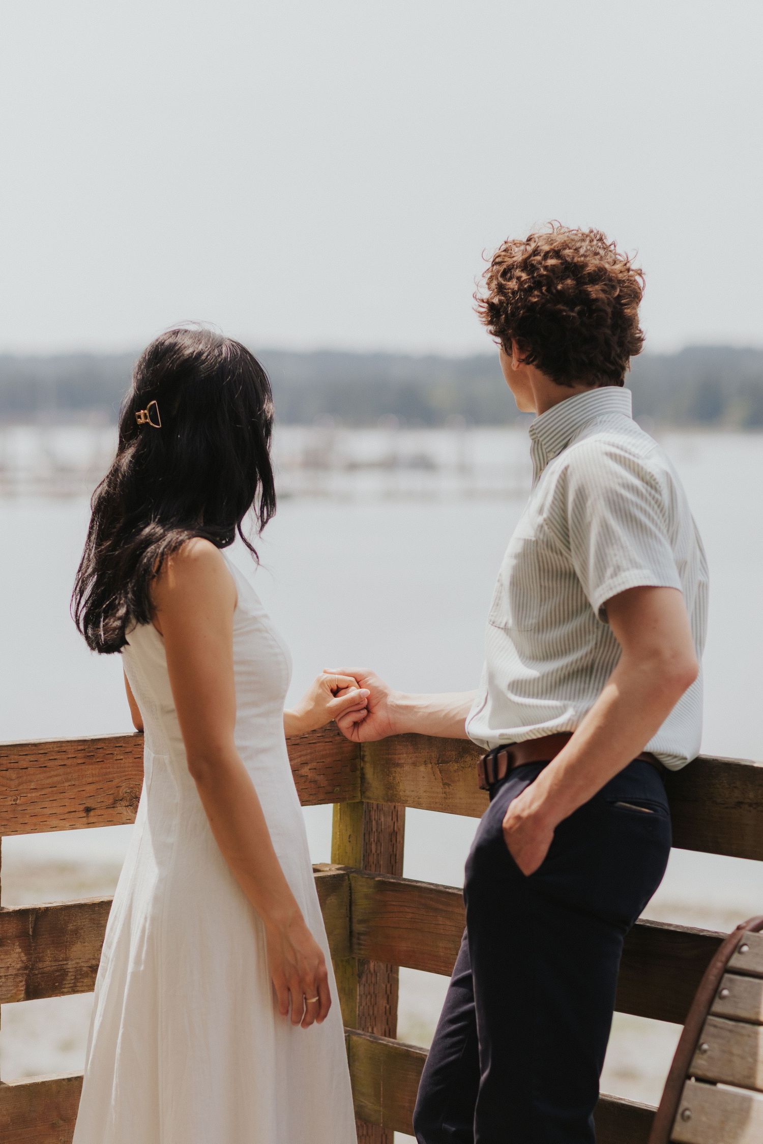 Couple in white and black attire sharing a romantic moment on wooden dock.