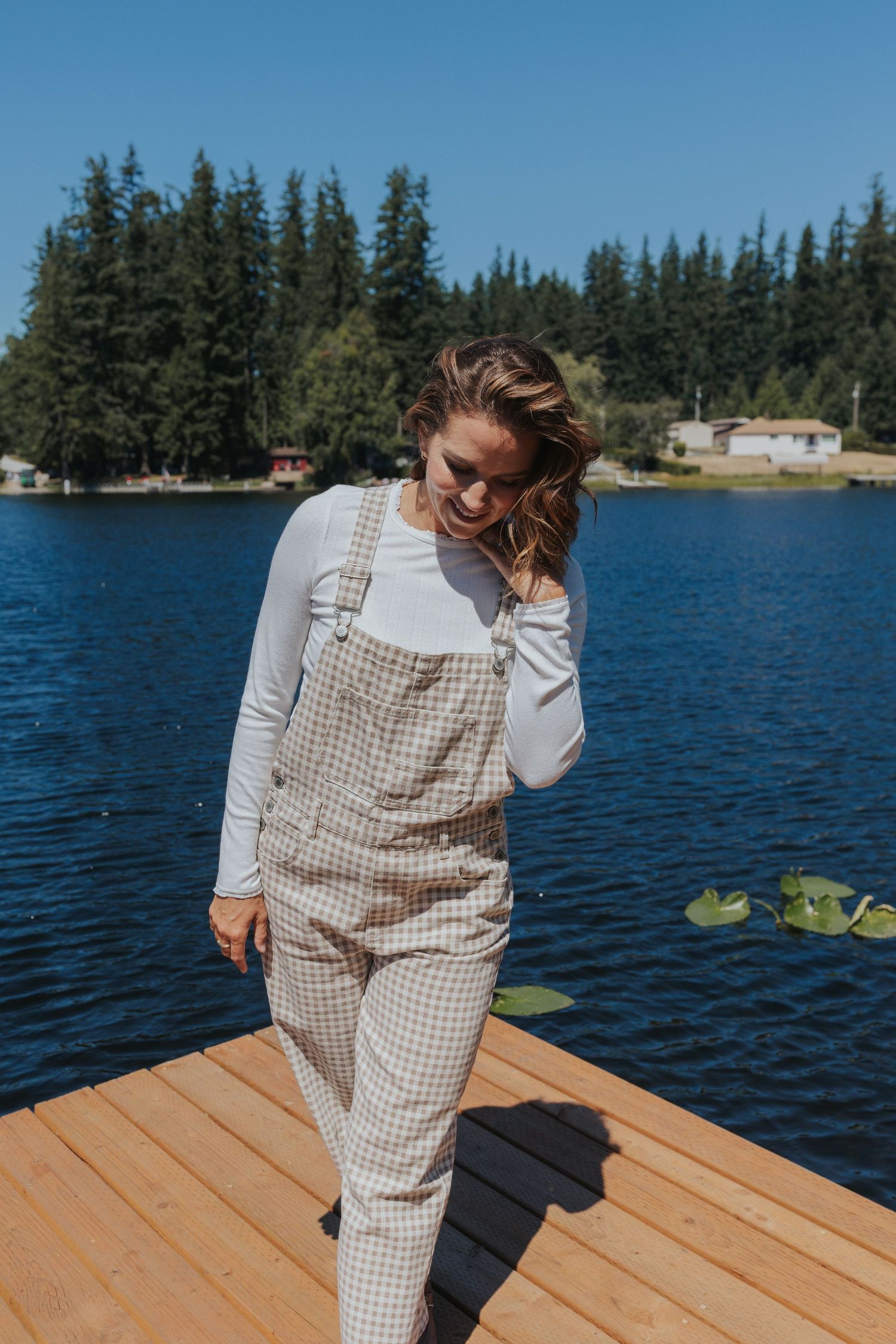 A person in gingham print loungewear dances playfully on a wooden dock by a lake.