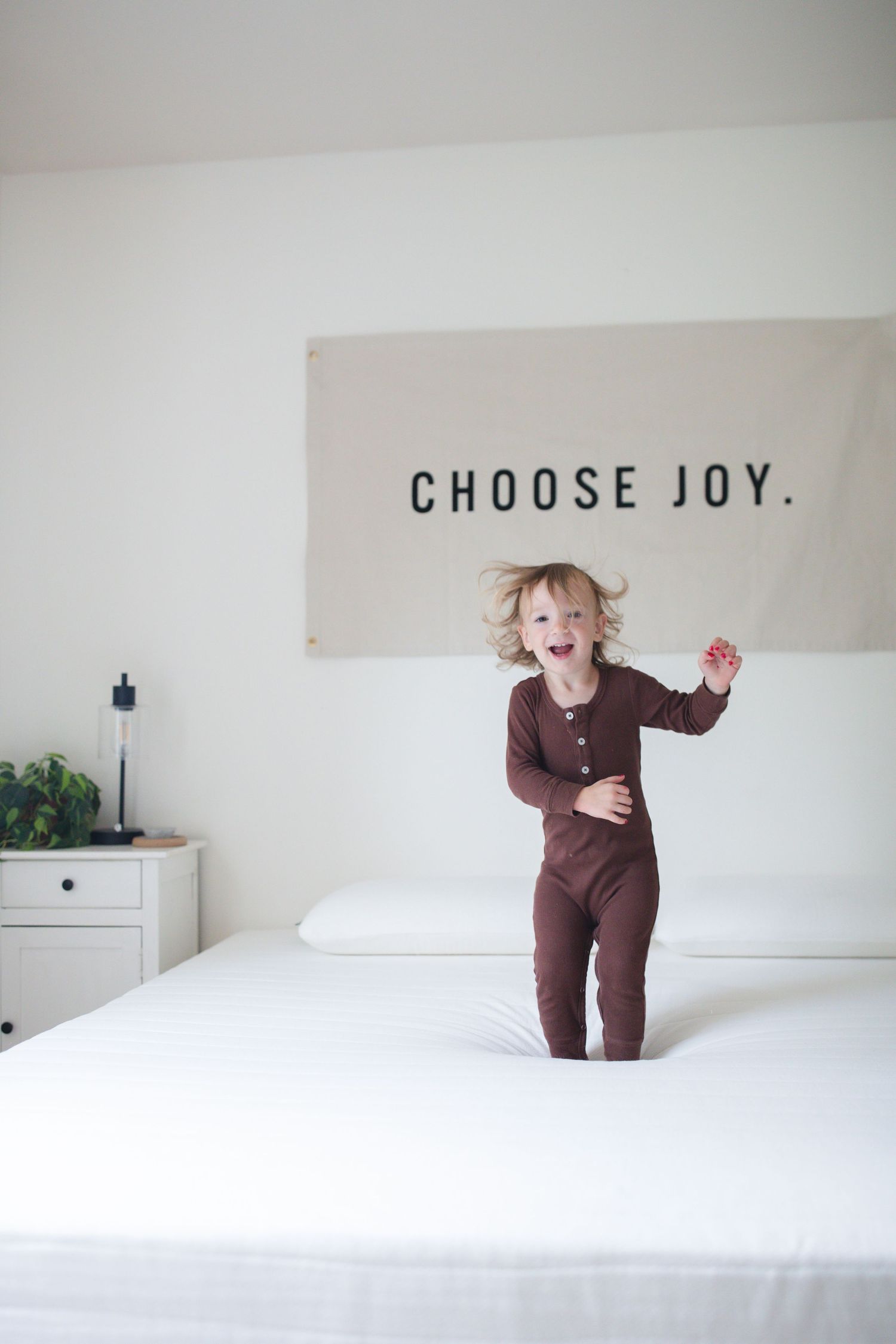 A minimalist white bedroom with 'CHOOSE JOY' text on the wall.