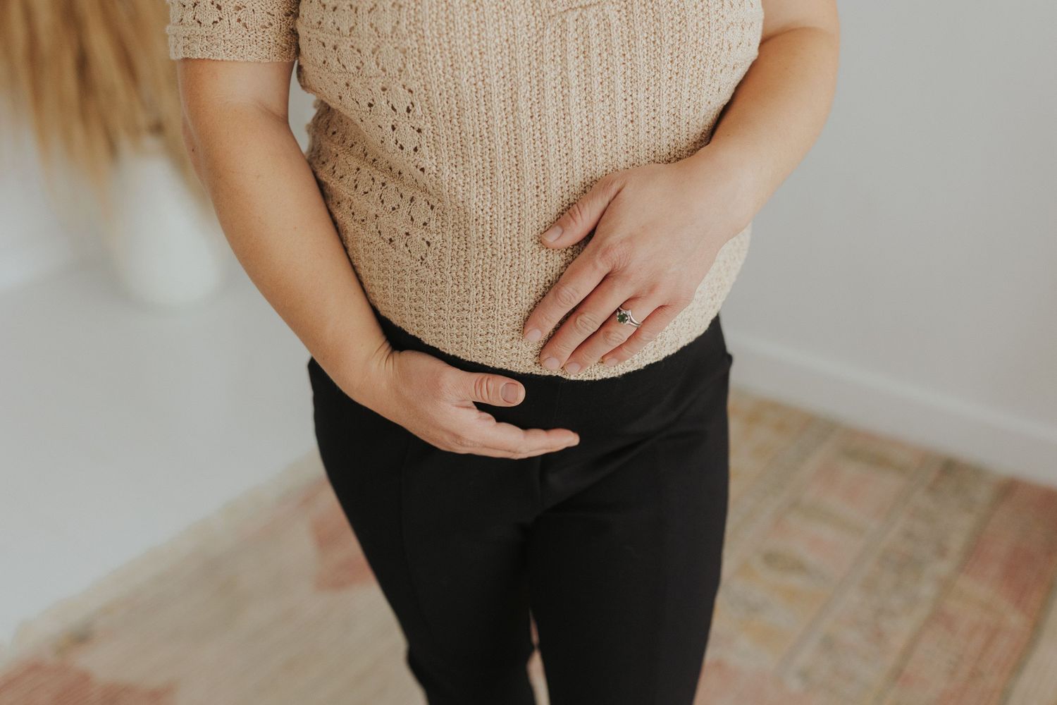 Close-up of cream knit sweater and black pants against white background.
