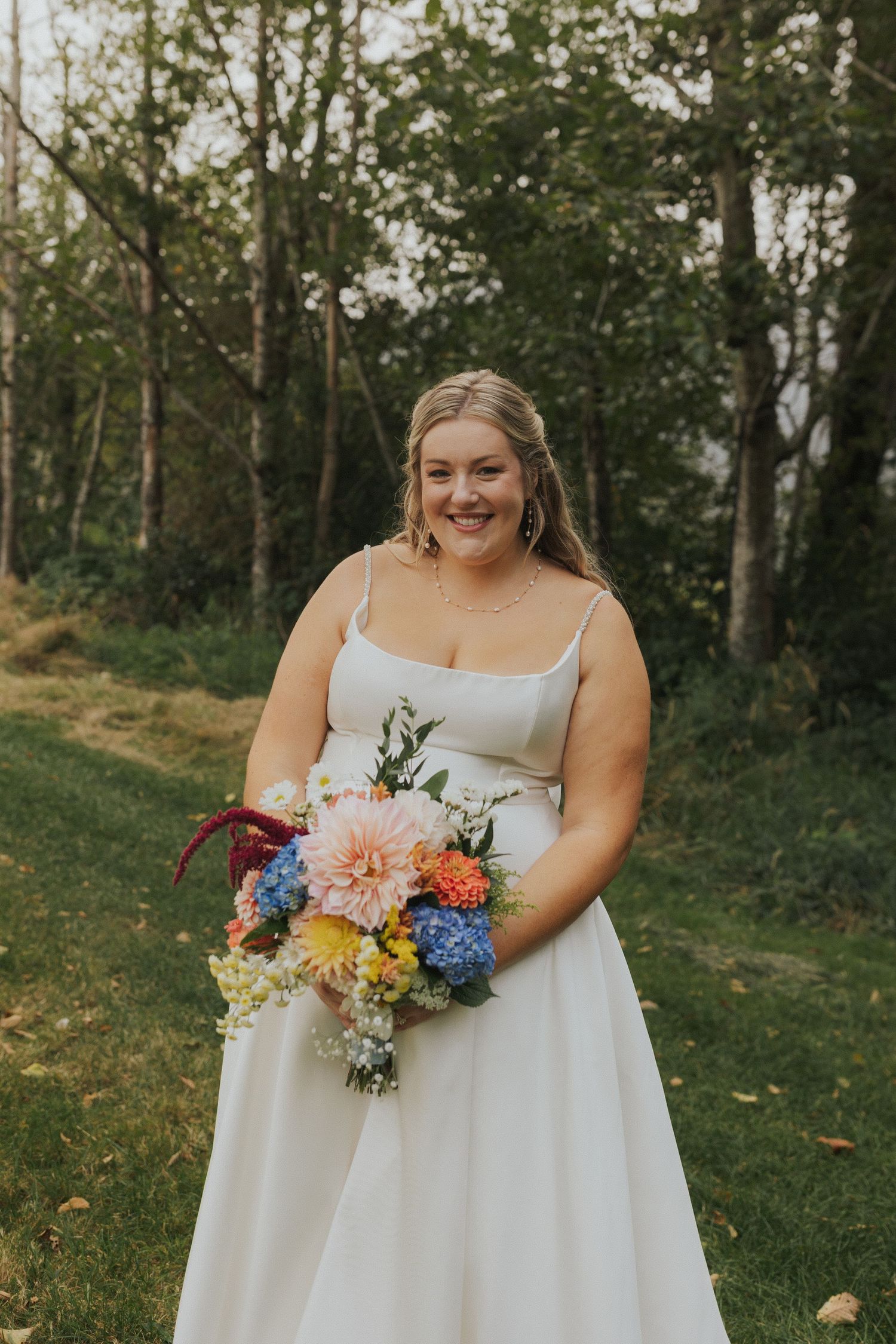 A bride in a flowing white dress holds a colorful bouquet with blue hydrangeas and coral flowers.