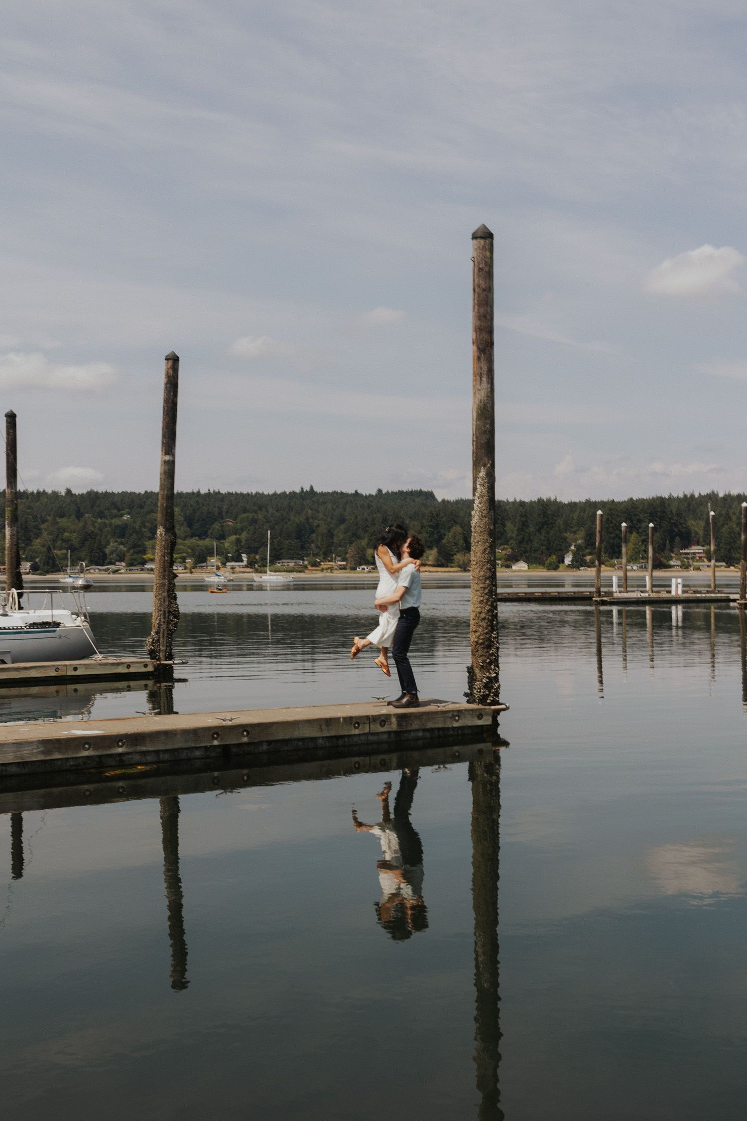 Wooden pier with posts stretching into calm water under cloudy sky.