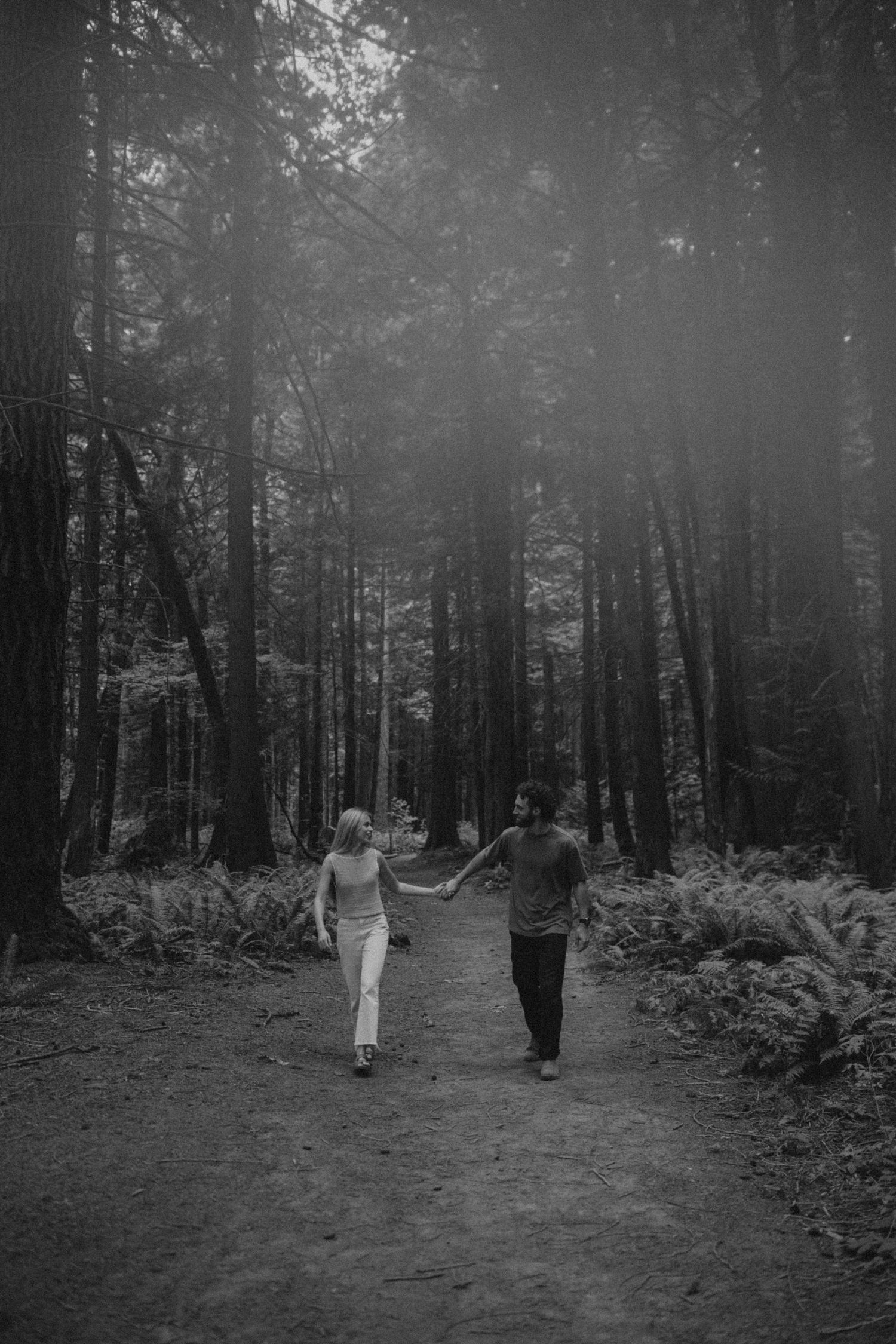 Two people strolling down a forest trail in black and white photography.