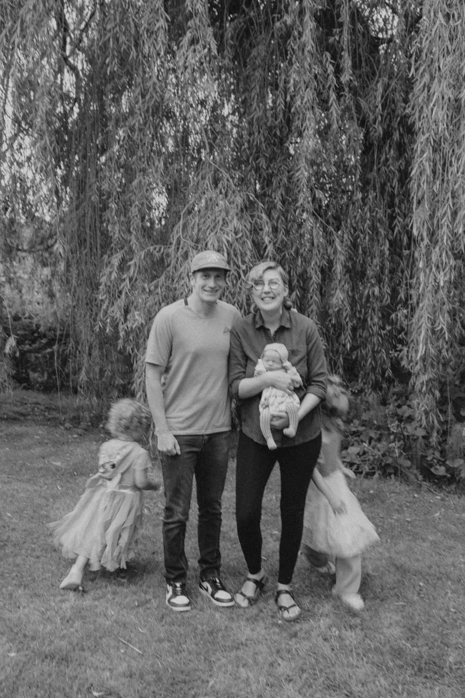 Family sitting together with their dog under a weeping willow tree in black and white.