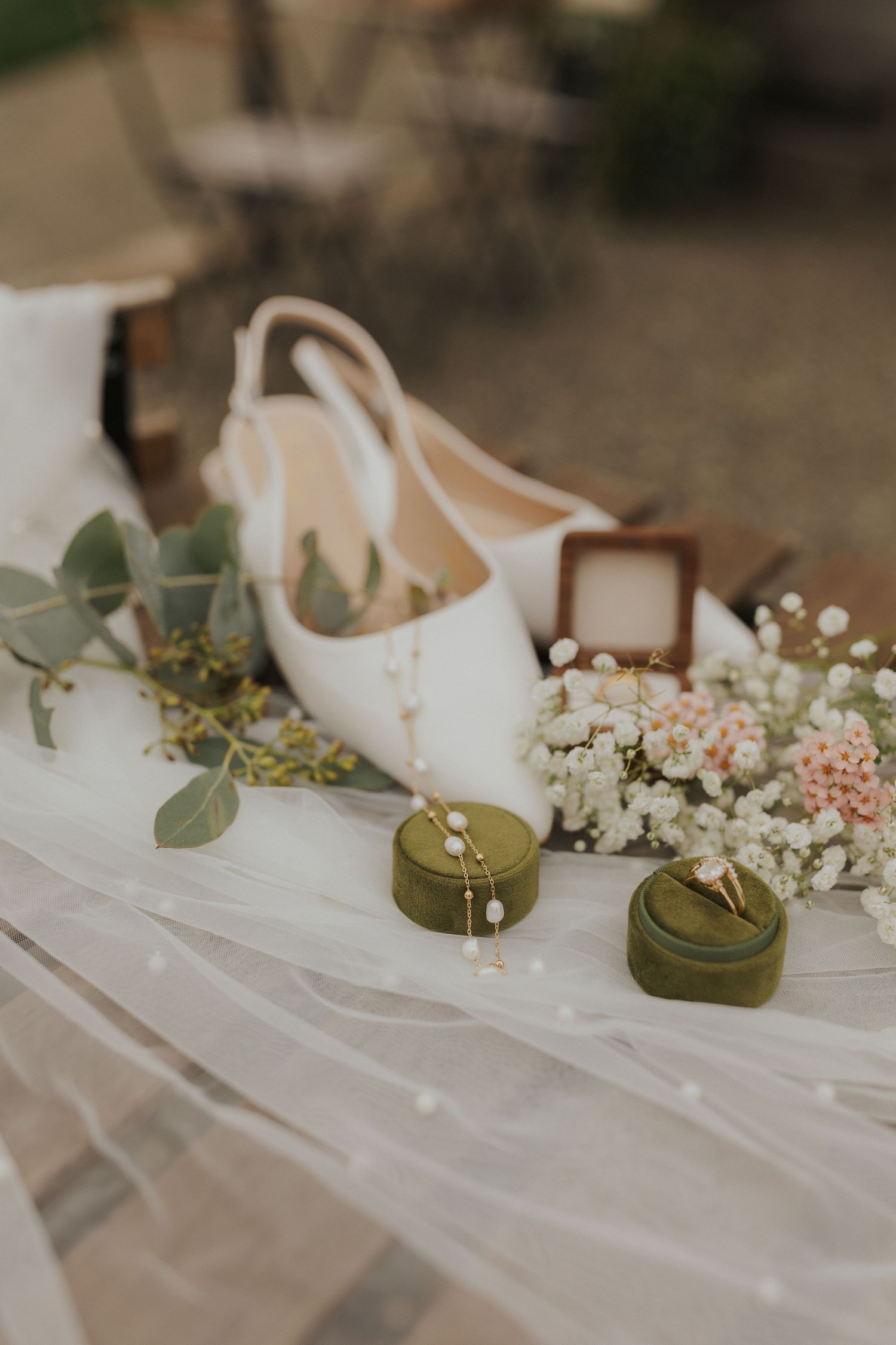 Wedding accessories including white shoes and delicate floral arrangements on white fabric.