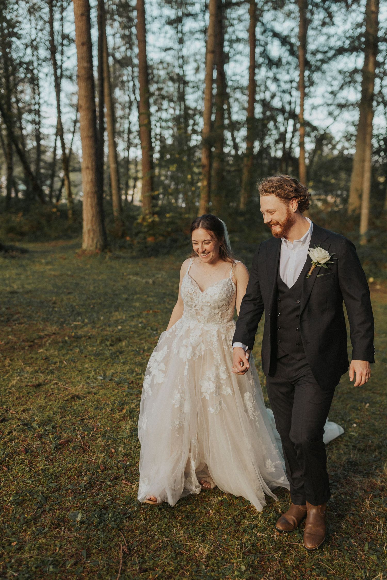 Newlyweds walking together through a pine forest at golden hour in elegant wedding attire.