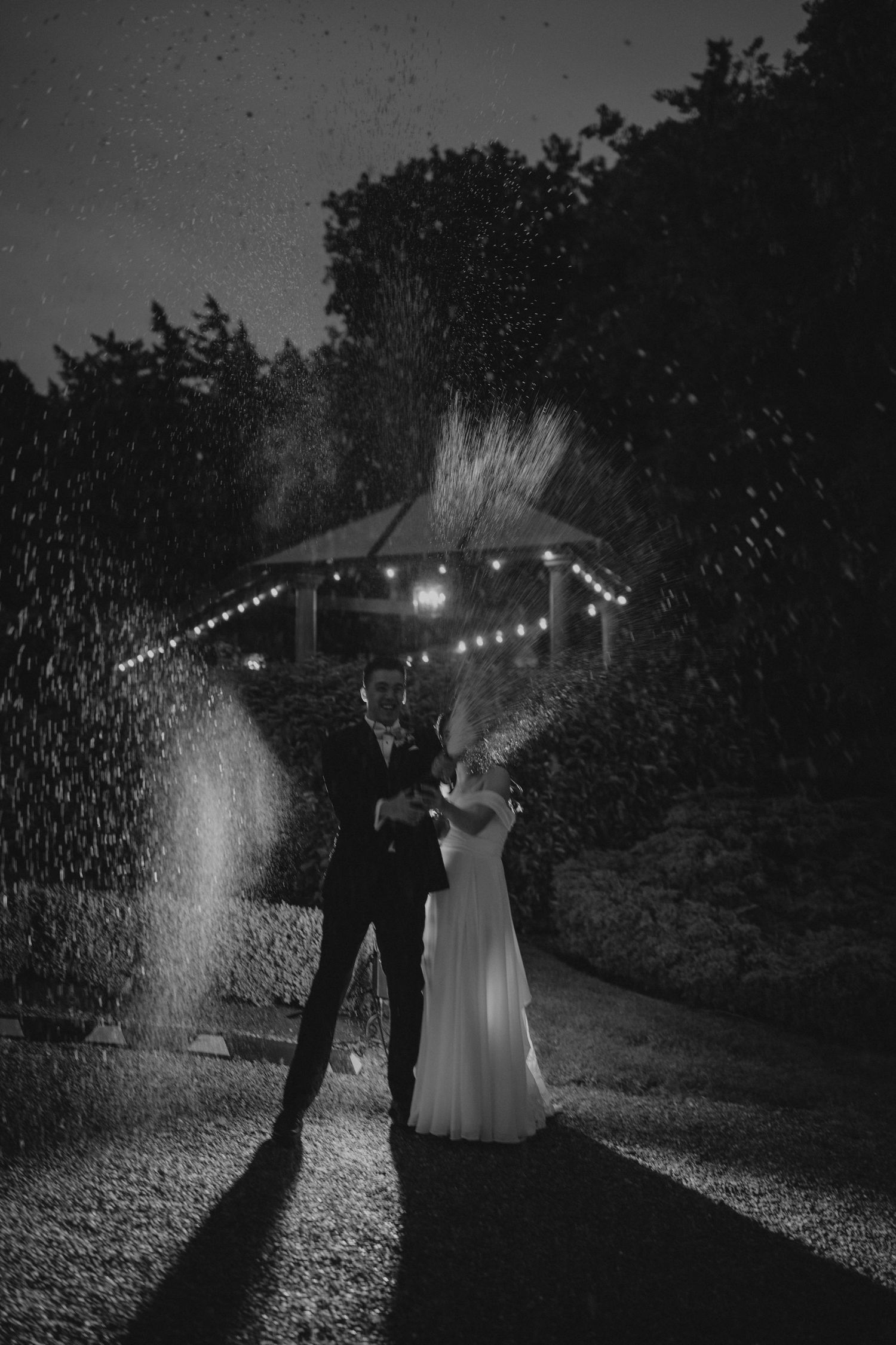 Dramatic black and white nighttime portrait with rain and string lights creating magical atmosphere.