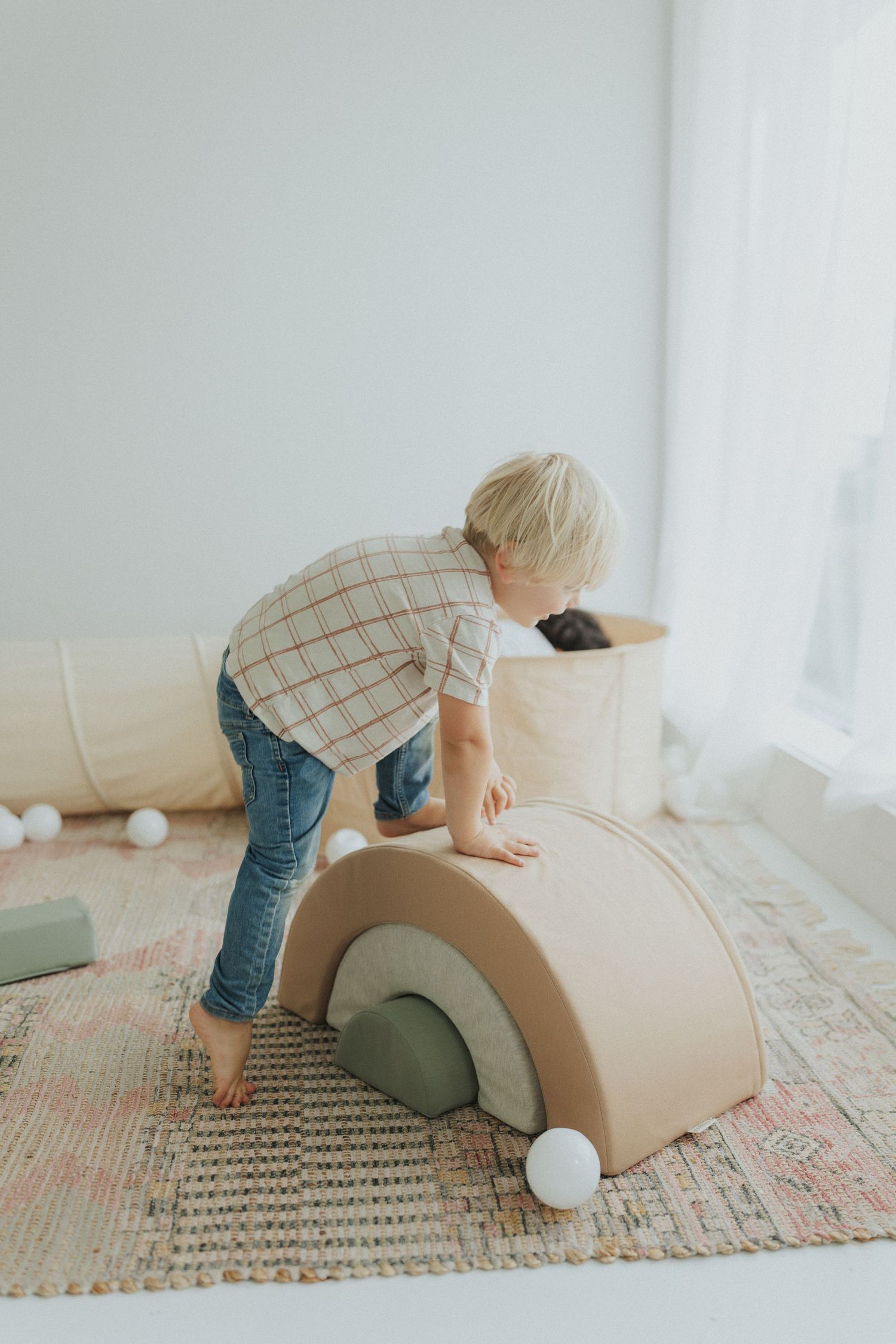 Curved foam play furniture on a patterned rug in a bright minimalist room.