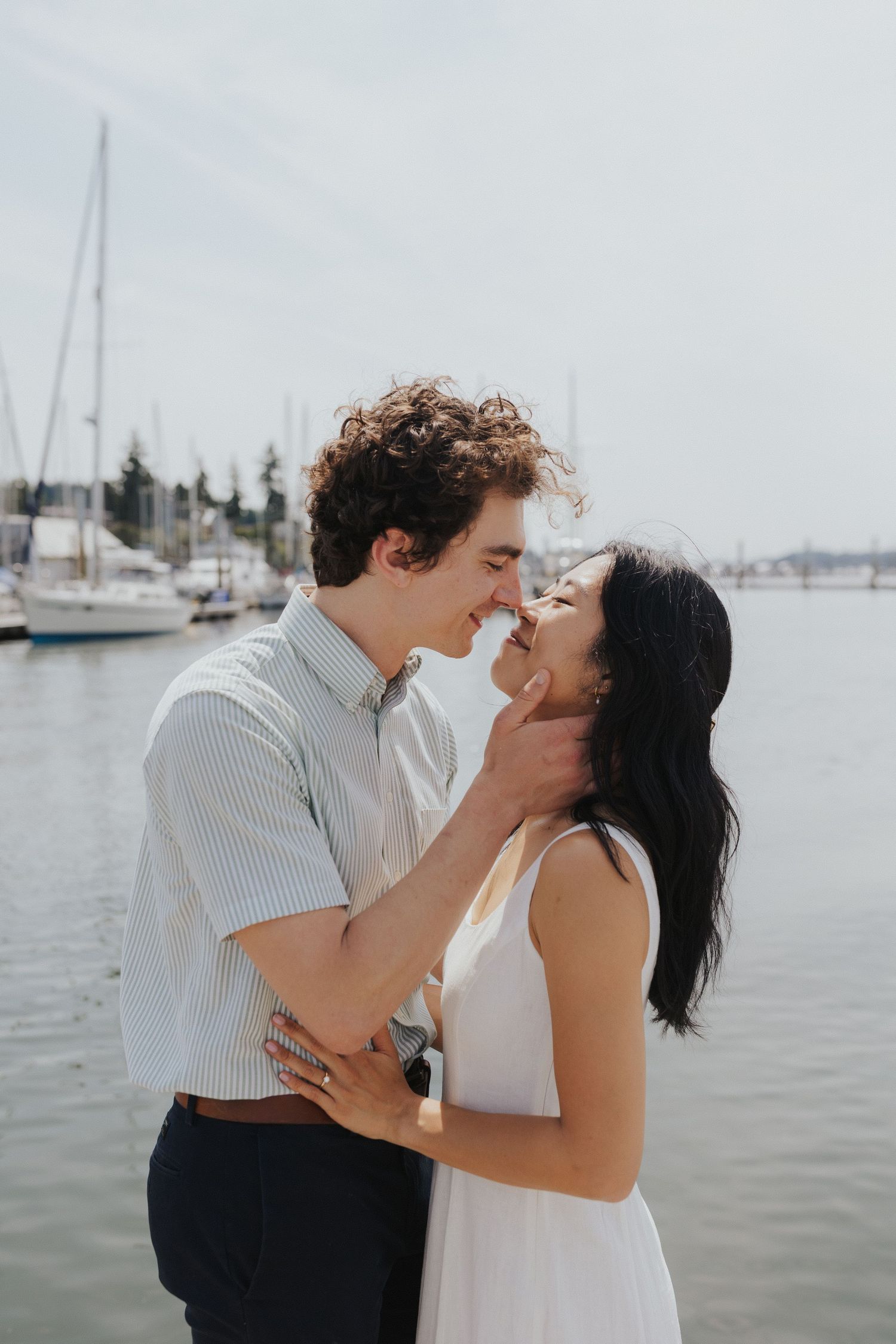 Intimate moment between couple at waterfront dock with boats in background.