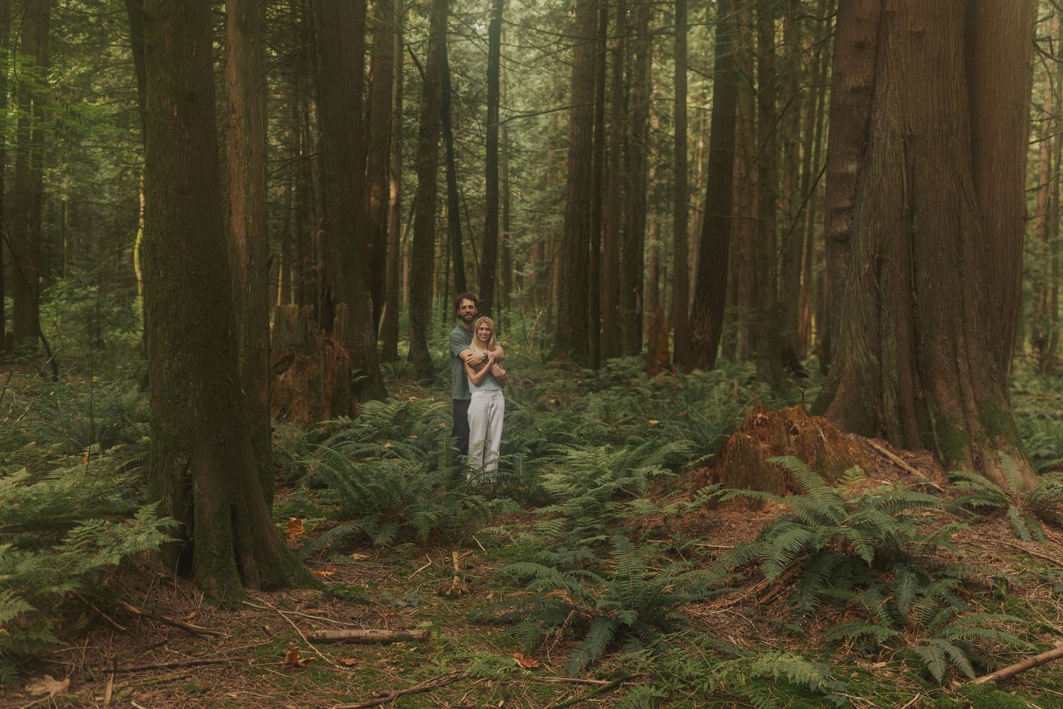 Couple enjoying a walk through a serene forest setting with towering trees.