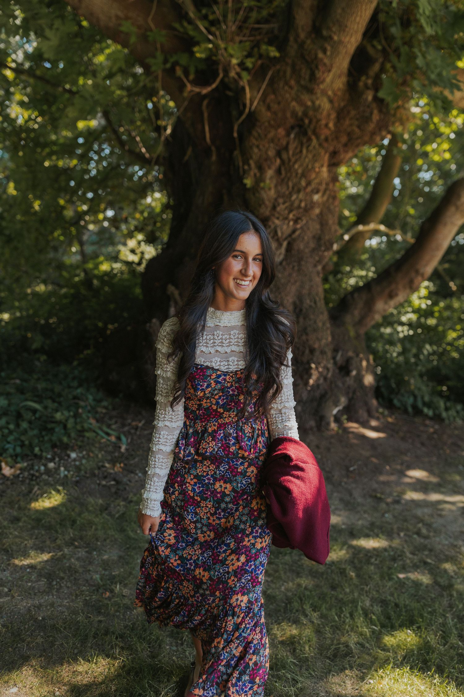A floral dress and white sweater ensemble photographed in a natural woodland setting.