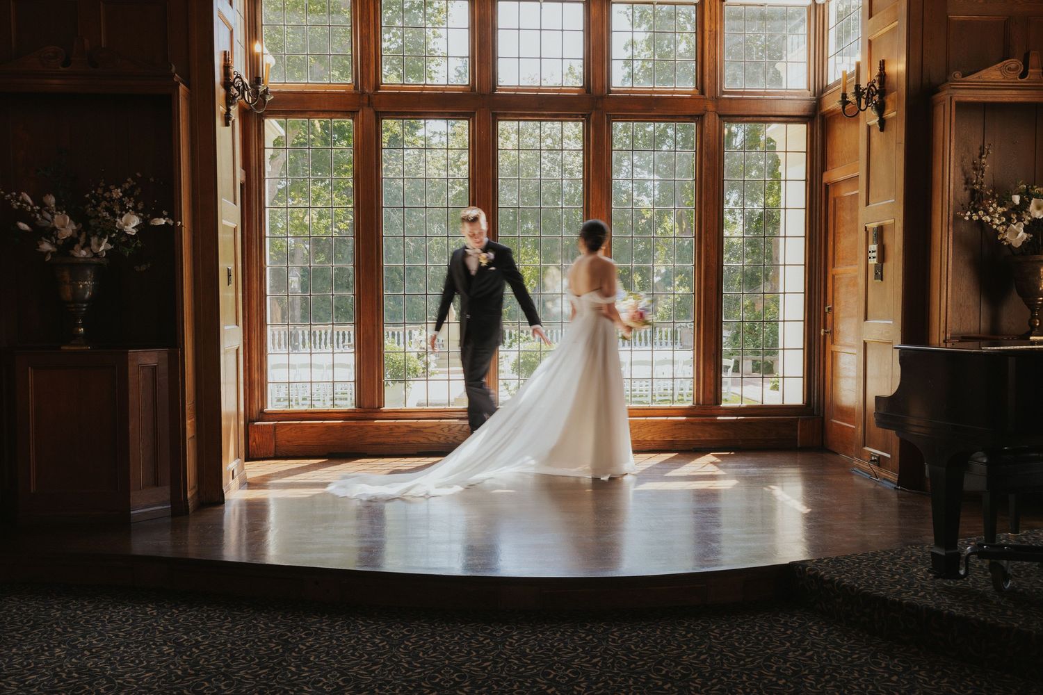 Wedding couple dancing on elevated platform in front of large vintage windows.