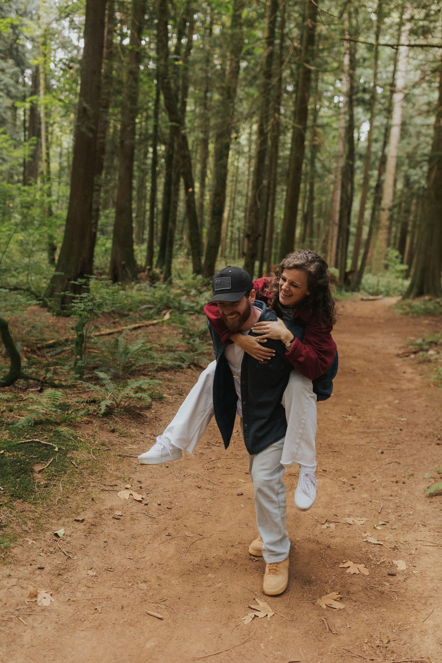 Playful couple dancing and spinning on a dirt trail through a peaceful forest.