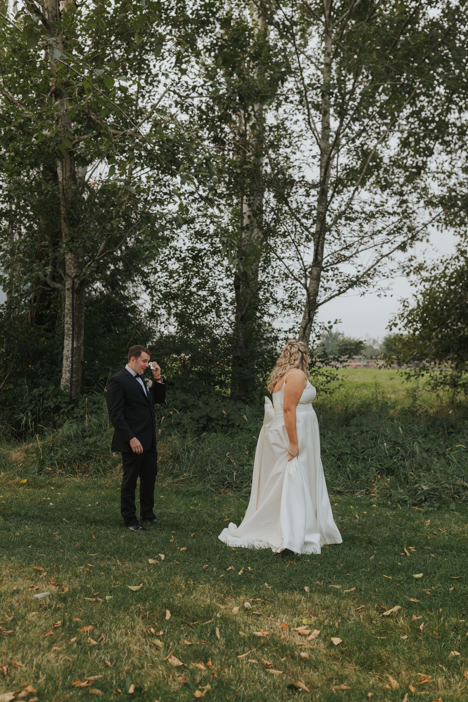 A wedding couple walks through a scenic outdoor setting with trees in the background.