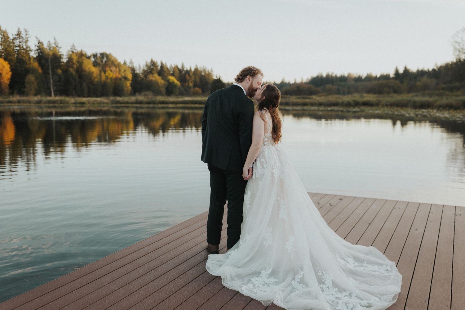 Romantic lakeside portrait with bride's dress train flowing across wooden deck.
