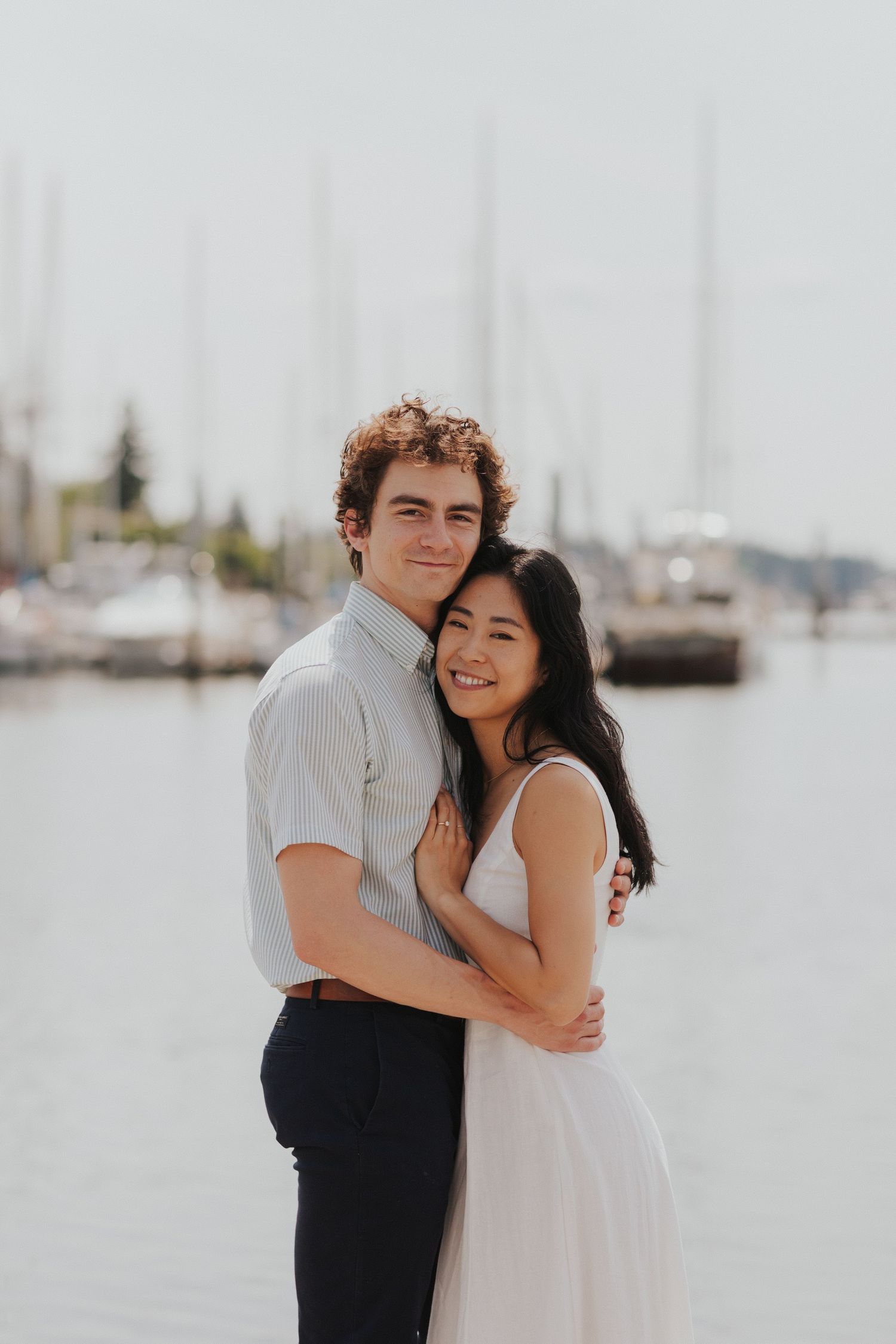 Happy couple laughing together at a marina with sailboats in the background.