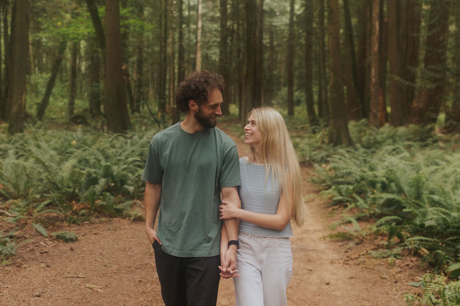 Romantic forest engagement session with couple walking through tall trees.