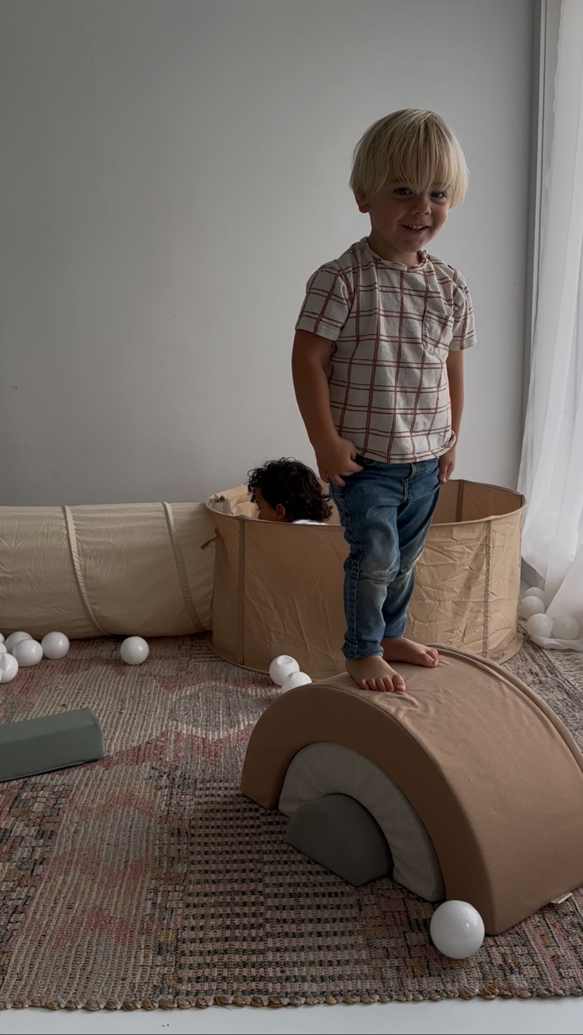 Child playing on brown cardboard toy car on patterned rug.