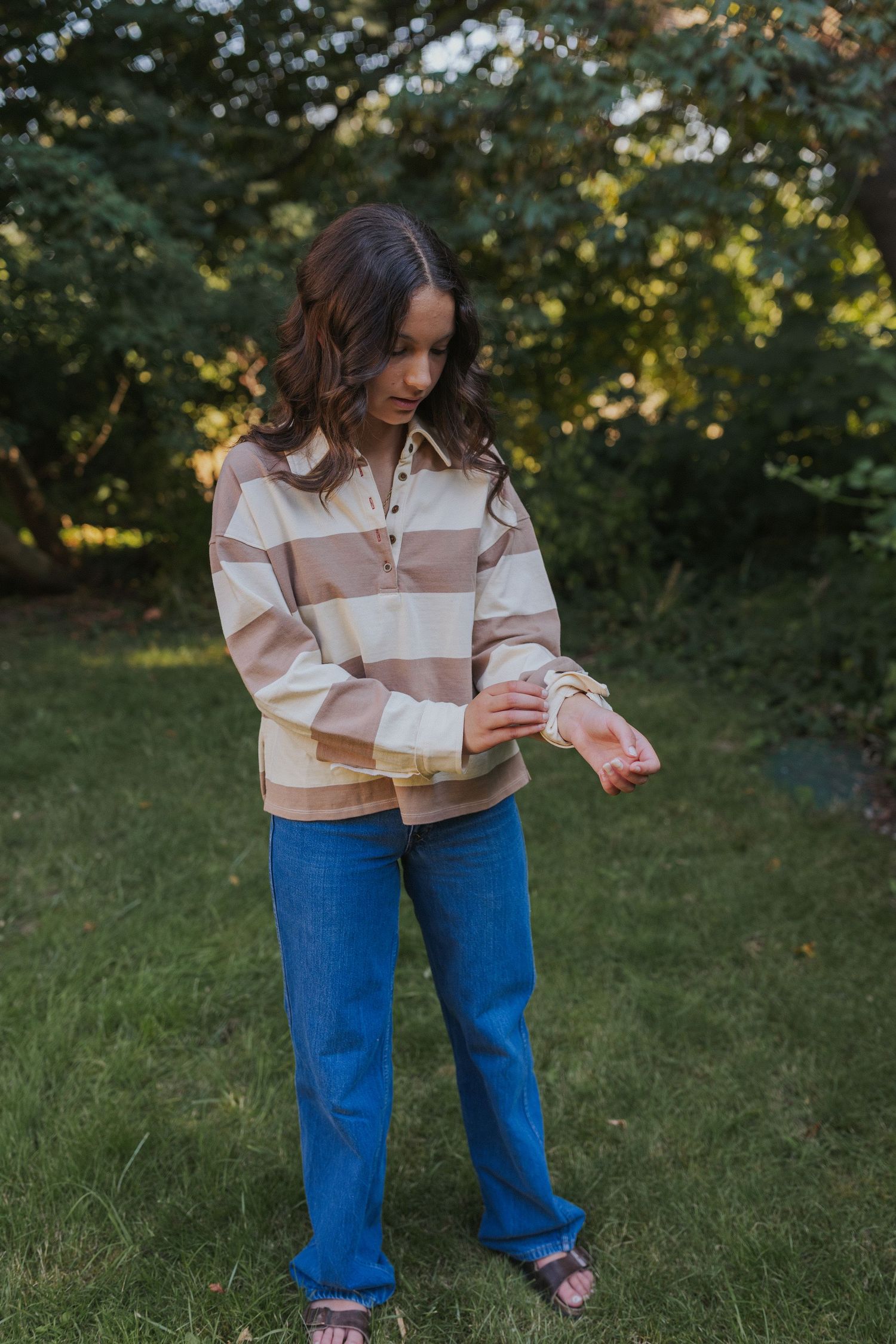 Person wearing striped sweater and blue jeans standing on grass in garden setting.