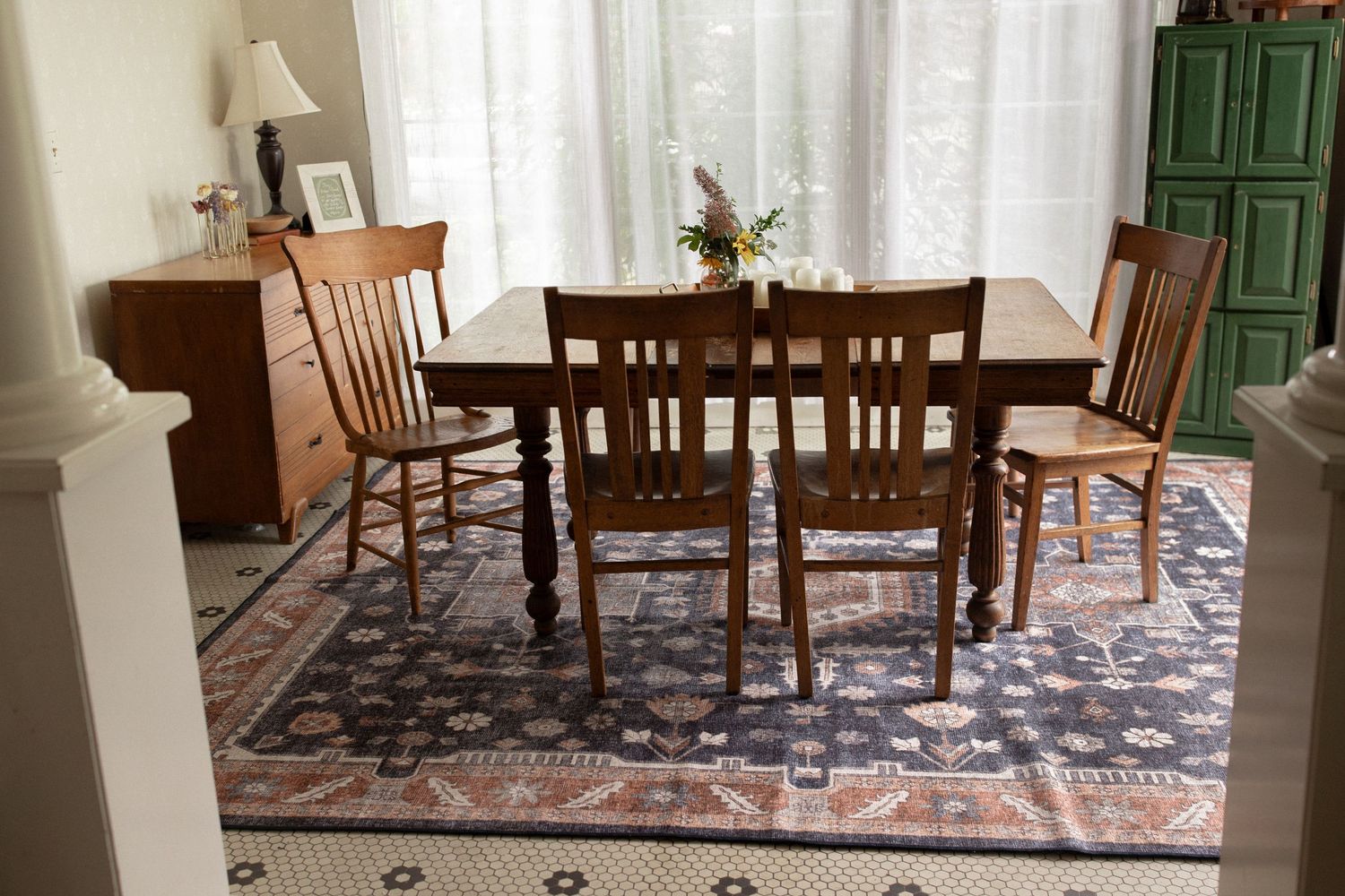 Dining room interior with wooden furniture, white curtains, and decorative area rug.