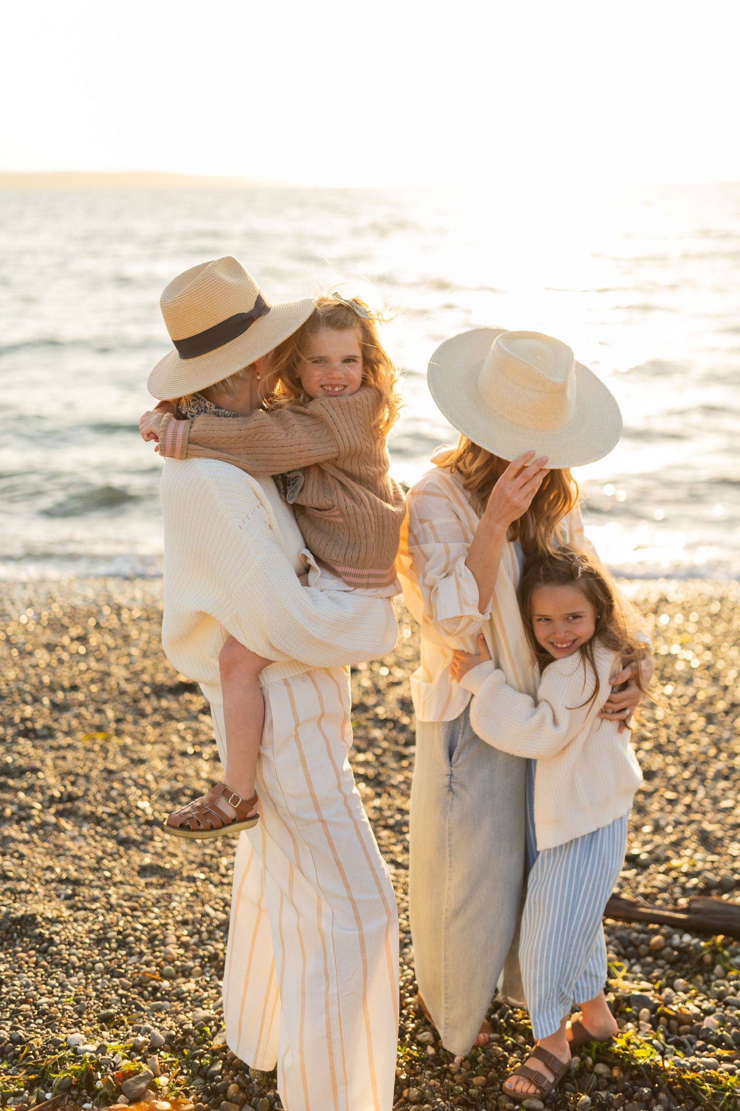 Family wearing neutral colors shares tender moments on sunset beach.