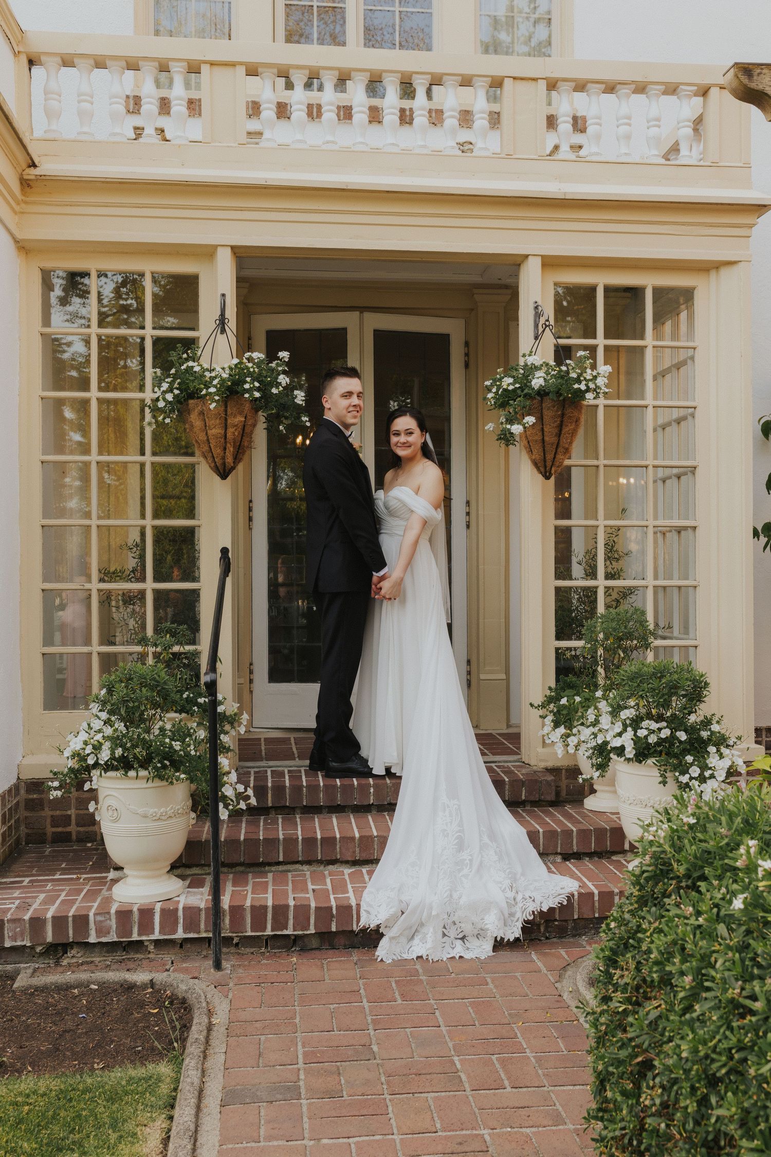 Wedding couple stands in front of elegant cream colored building with large windows.