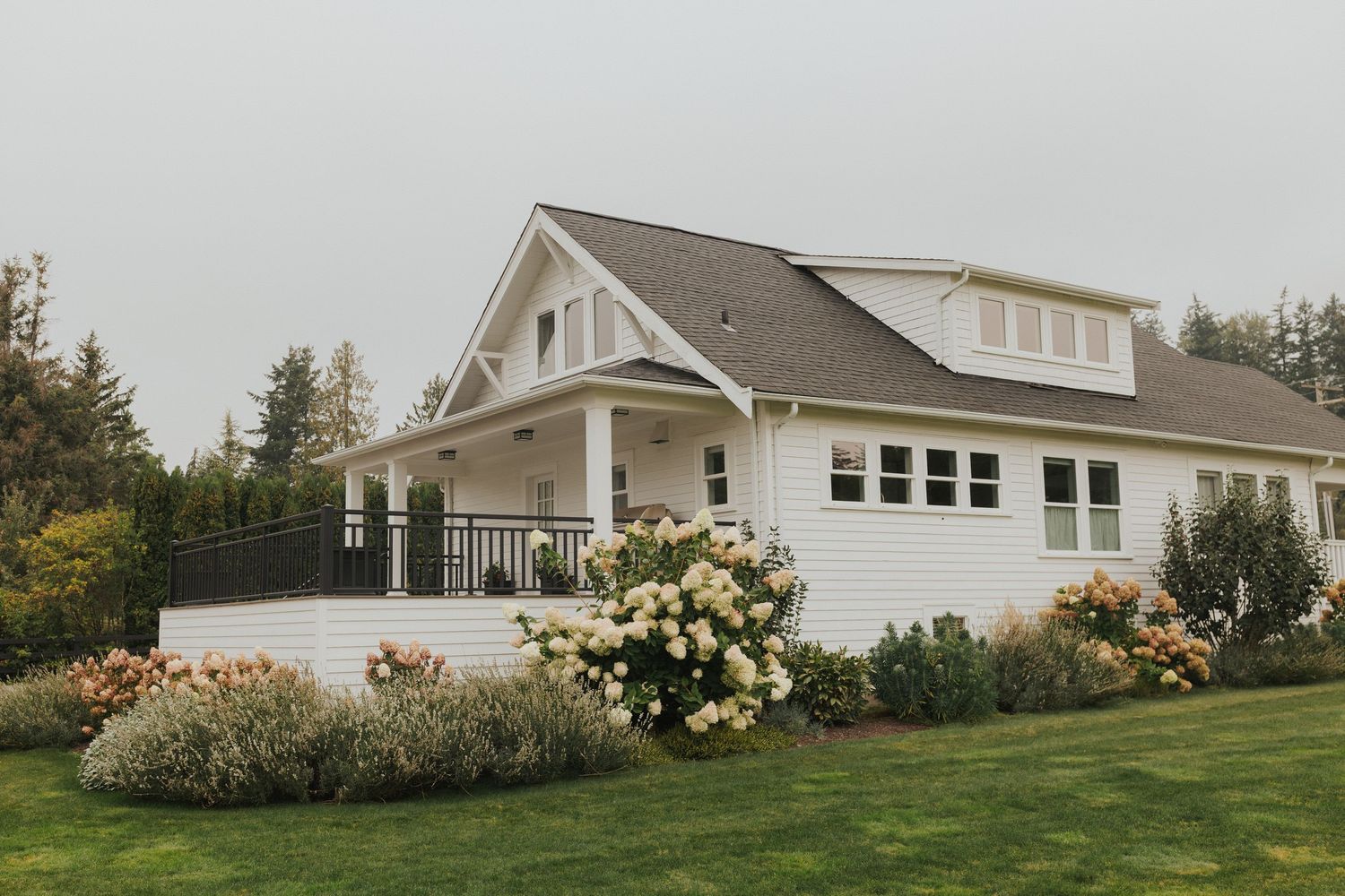 Panoramic view of a white farmhouse with landscaped gardens and blooming flowers.