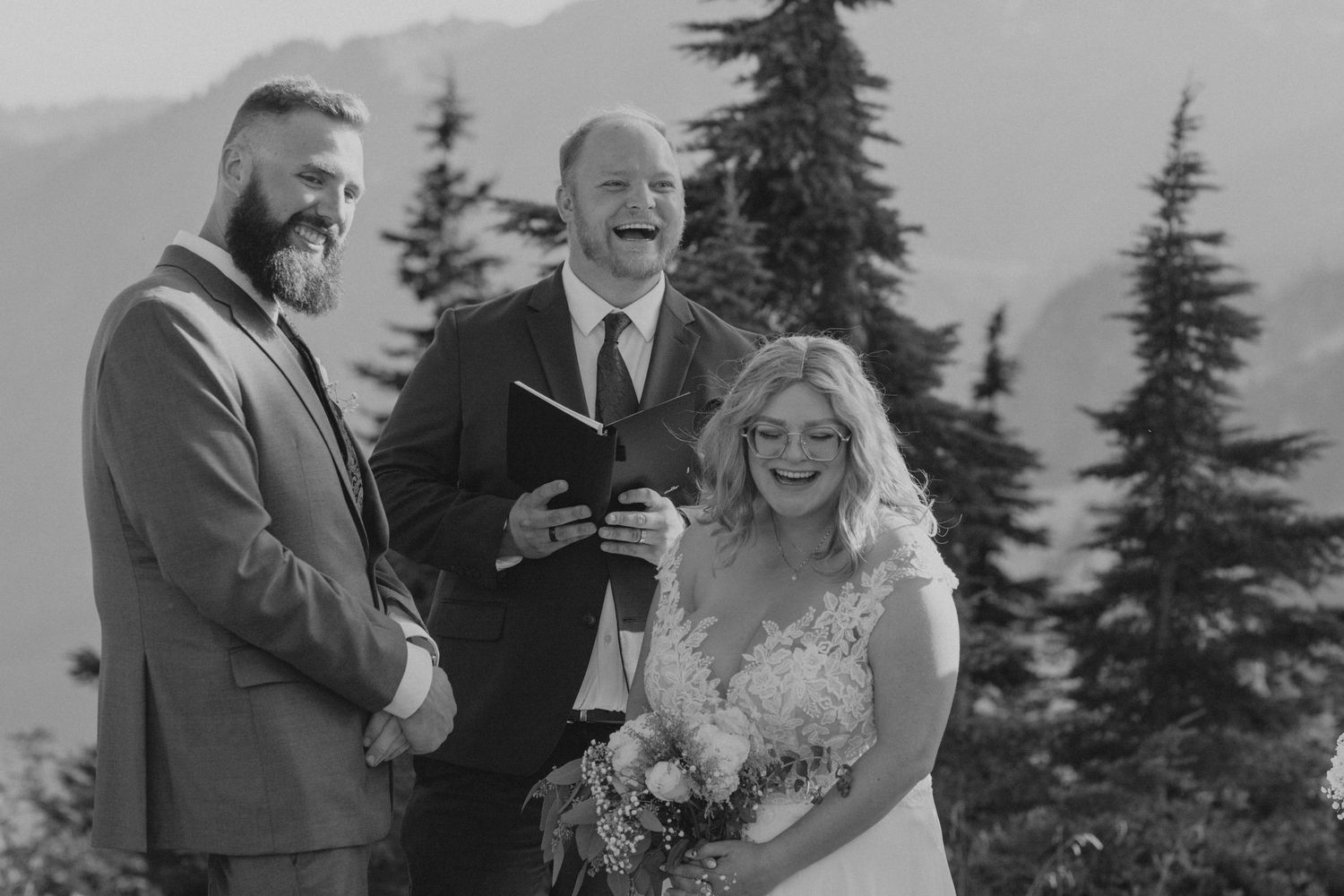 A wedding ceremony unfolds against a stunning mountain landscape with evergreen trees.