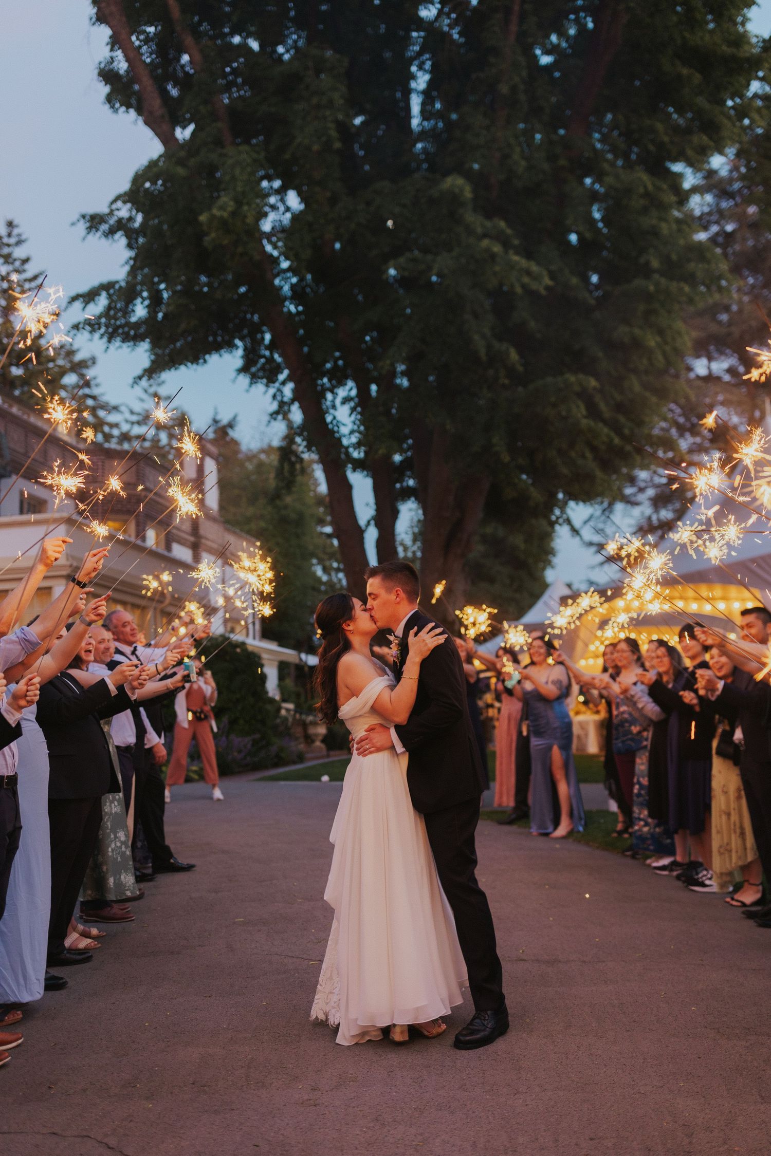 Wedding sparkler exit with guests lining pathway at dusk creating magical celebration moment.