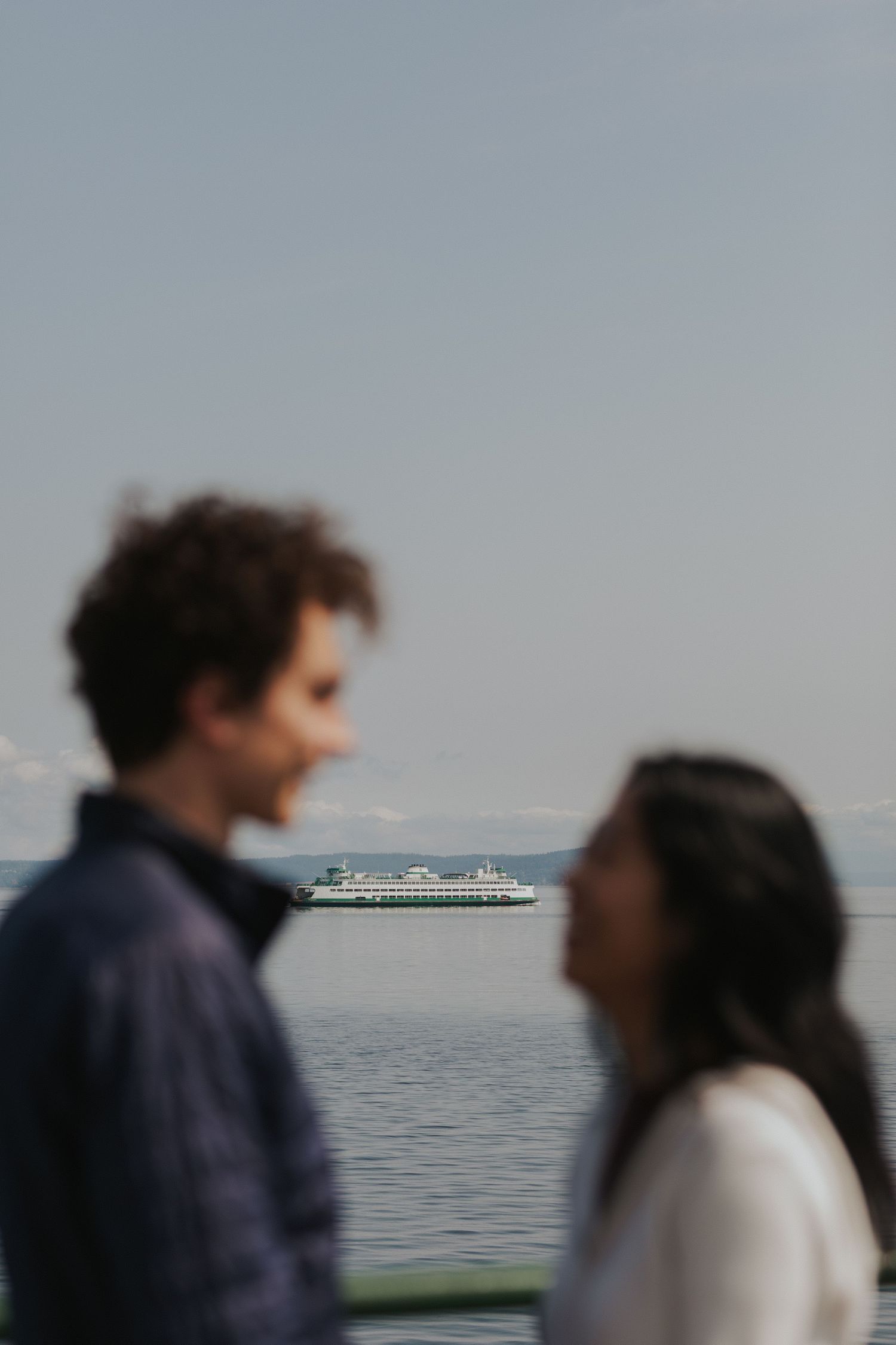 Silhouetted figures on ferry deck with cruise ship visible in distance.