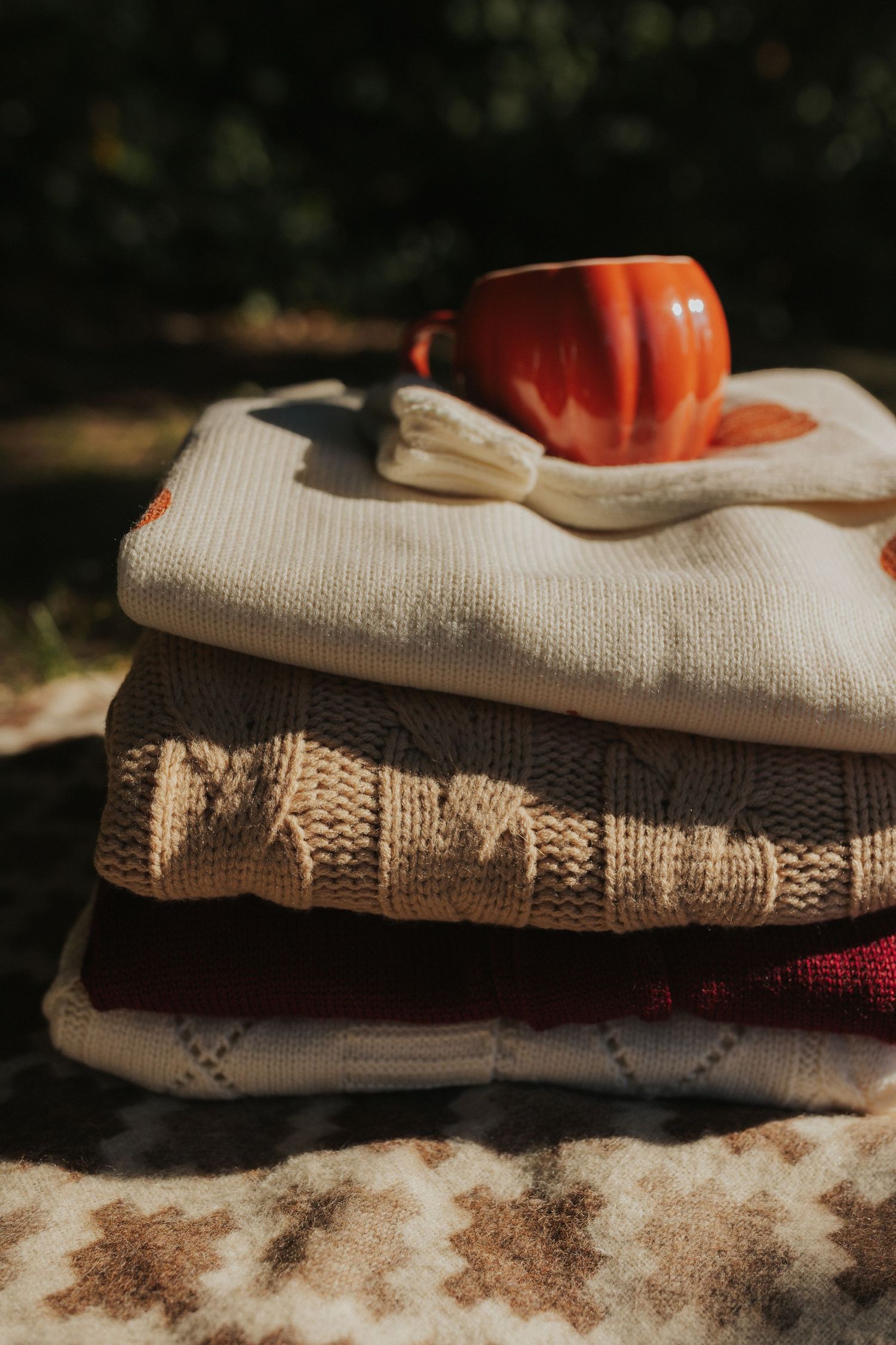 Folded sweaters and textiles with a decorative orange pumpkin on top in outdoor lighting.