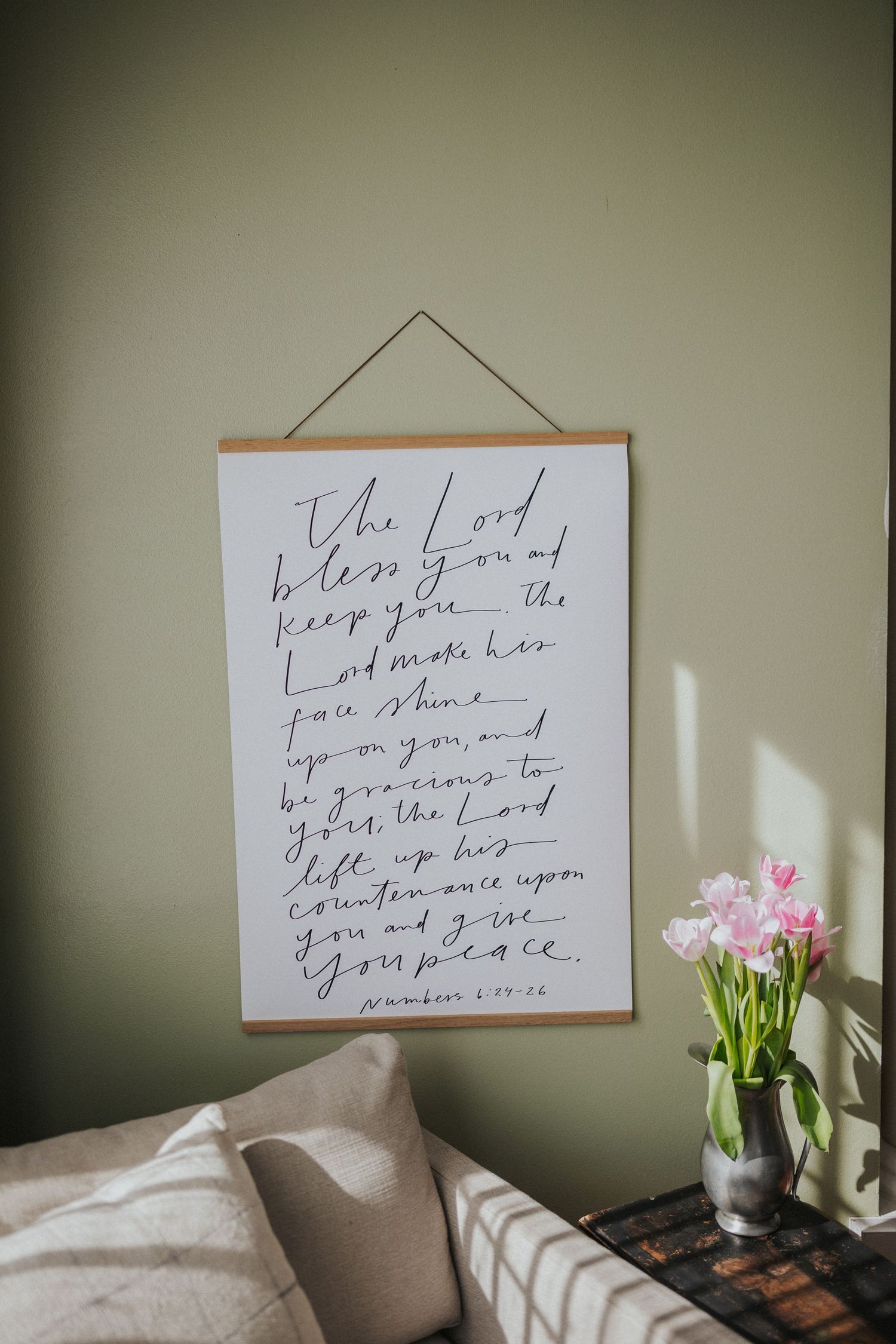 Handwritten inspirational quotes framed on sage green wall with pink tulips in vase.