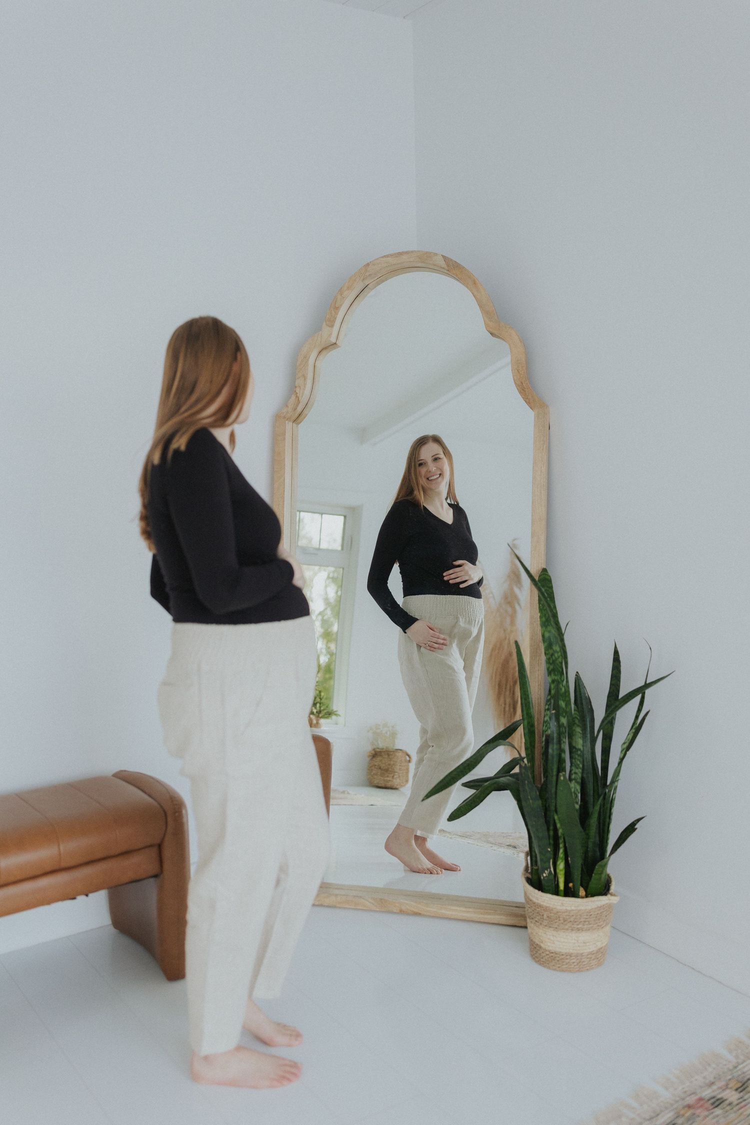 Minimalist white room interior with wooden mirror and potted plant against light walls.