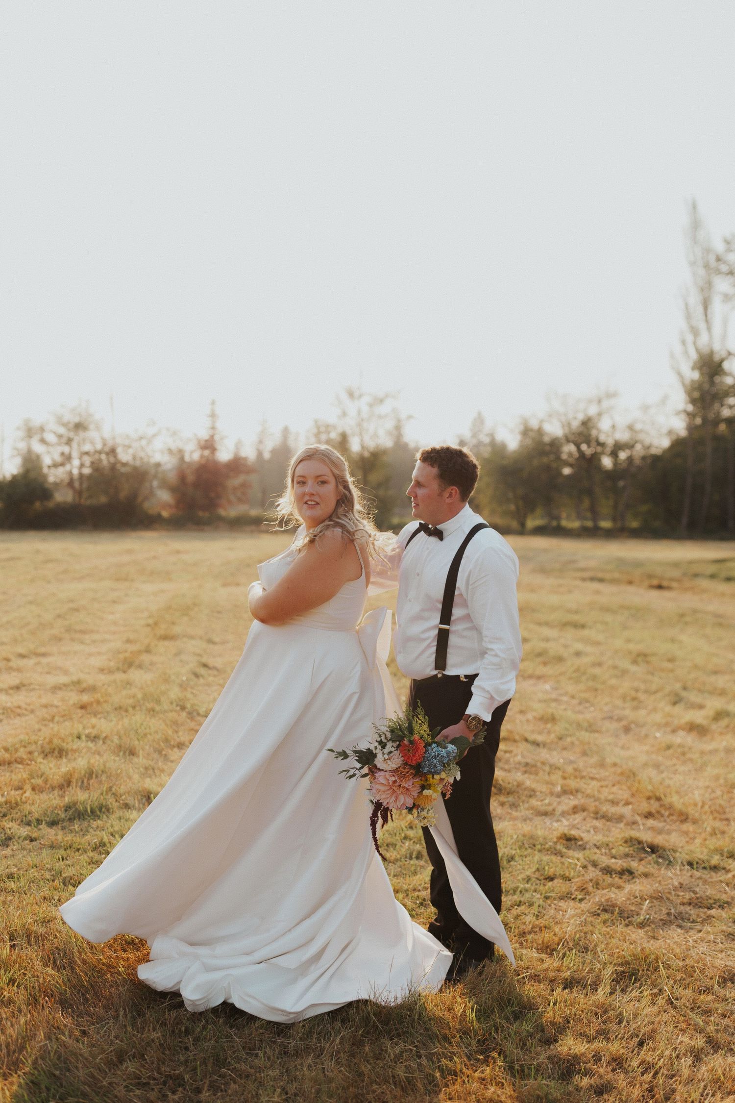 Wedding couple strolling through a golden field with colorful bouquet at sunset.