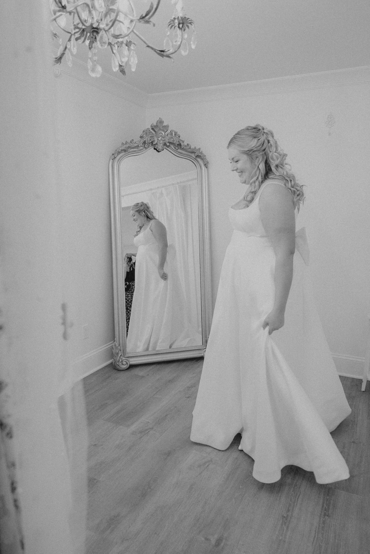 Black and white photo of wedding gowns displayed in a bright room with hardwood floors.