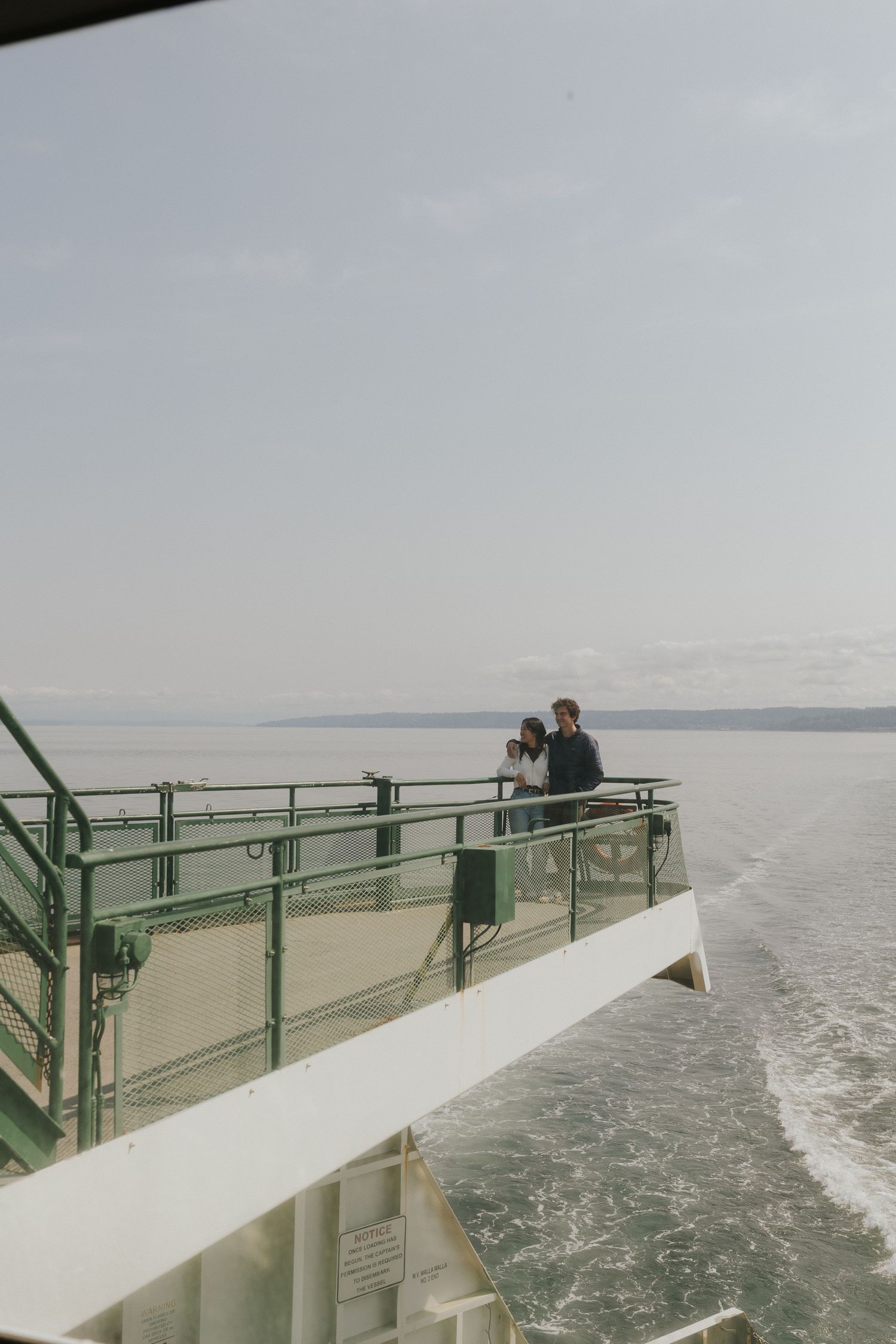 Side view of a couple enjoying the view from a ferry boat's outdoor observation deck.