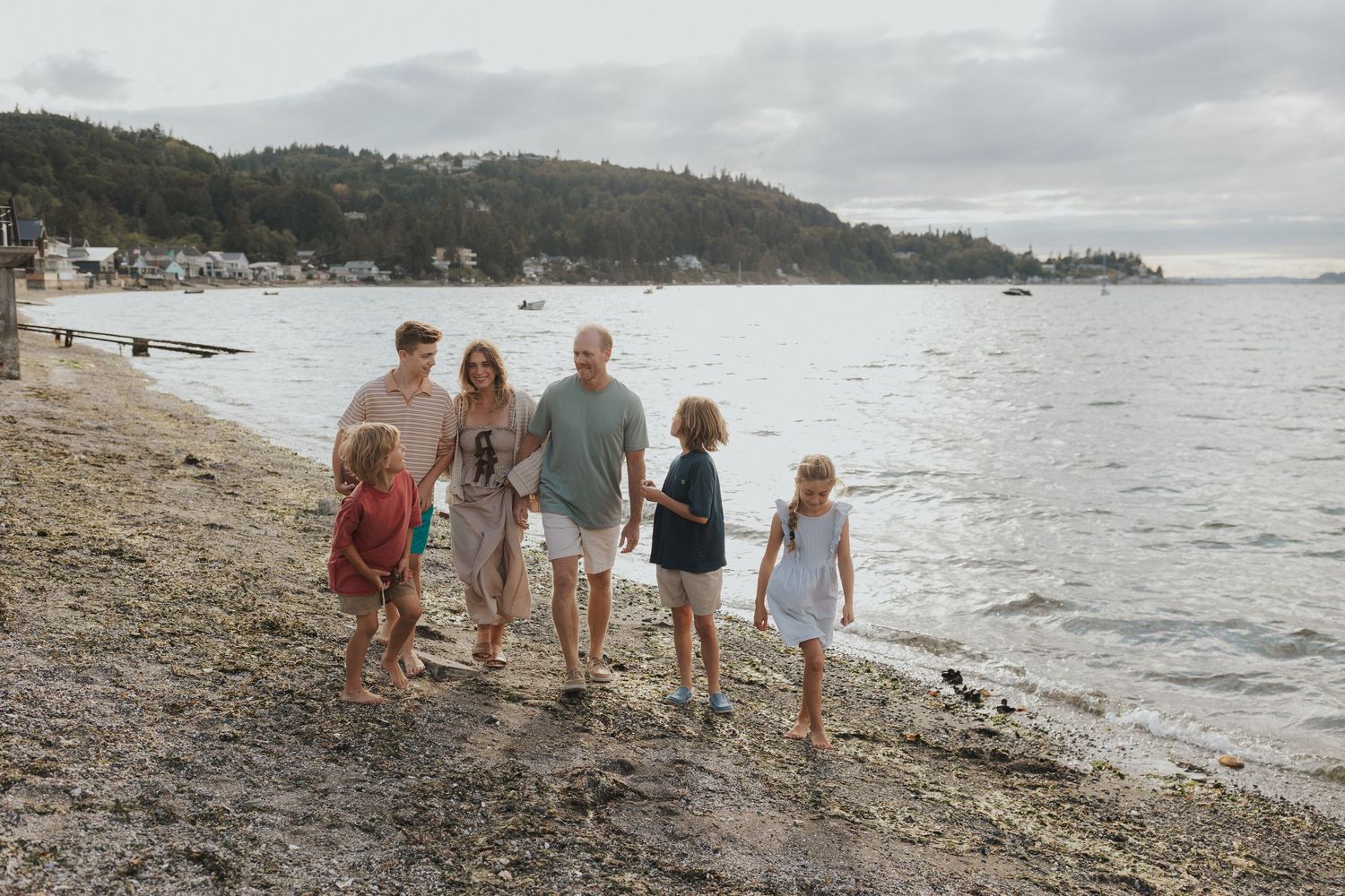 Family members exploring a pebble beach with forested hills and water views.