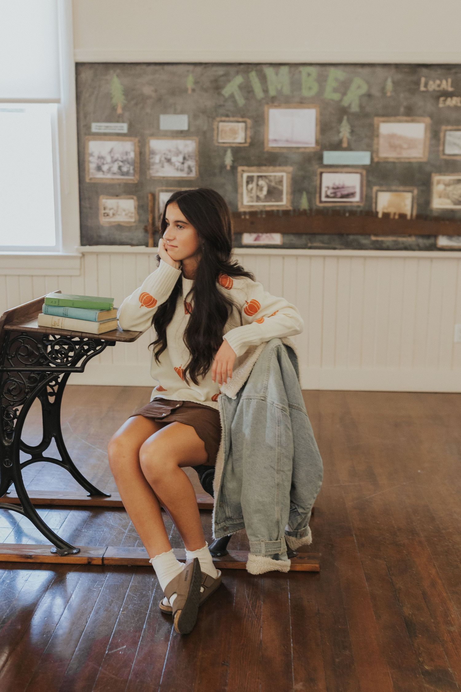 Student sitting at antique school desk in historic classroom with photos on wall.