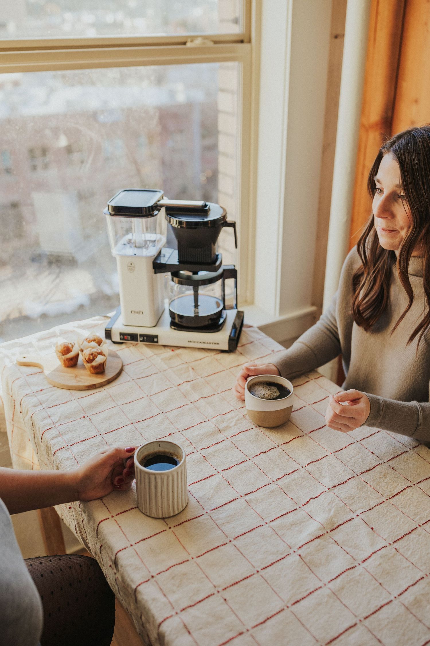 Coffee and pastries arranged on a checkered tablecloth with morning sunlight streaming through the window.