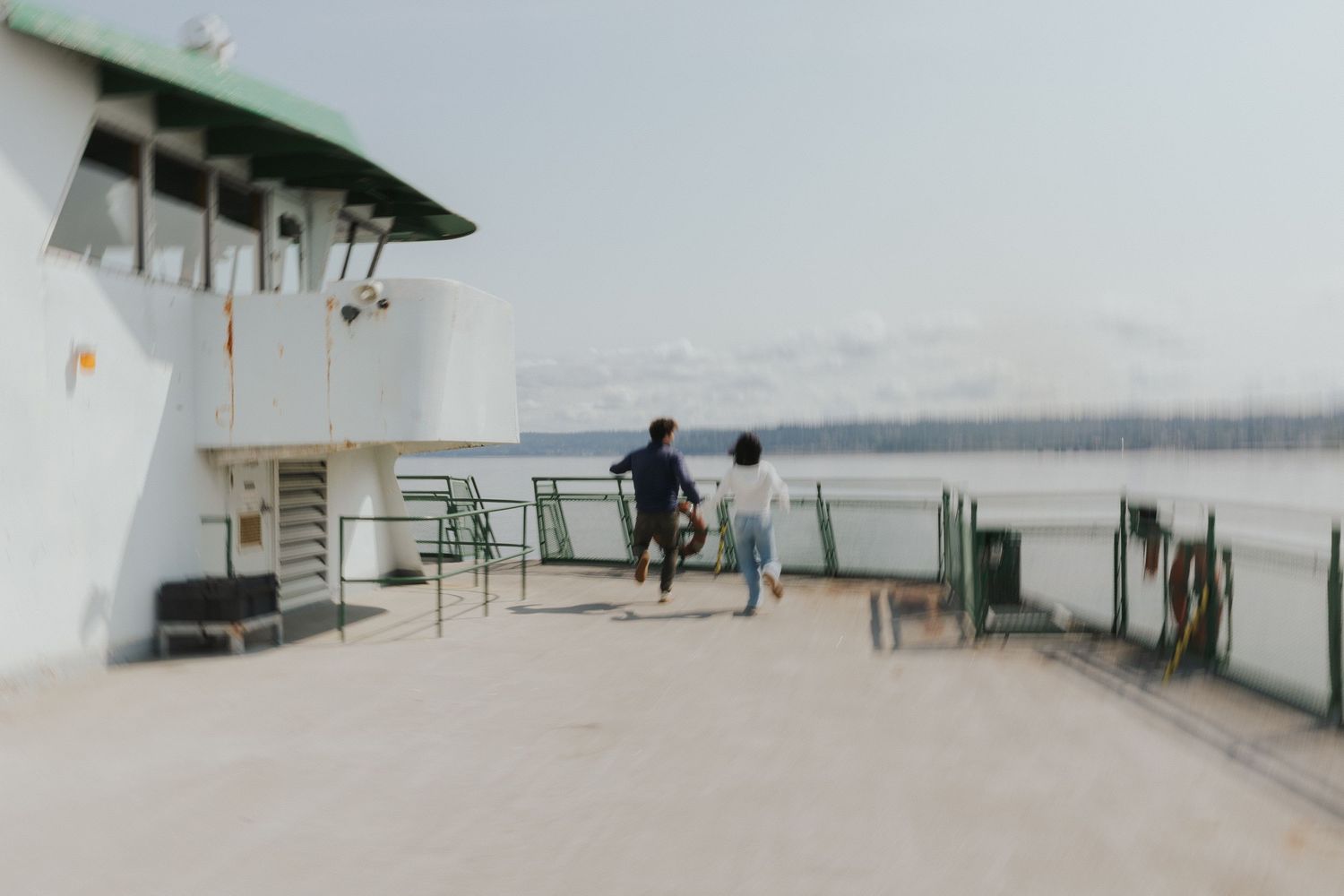 Two figures stand on the deck of a ferry boat overlooking the water on a misty day.