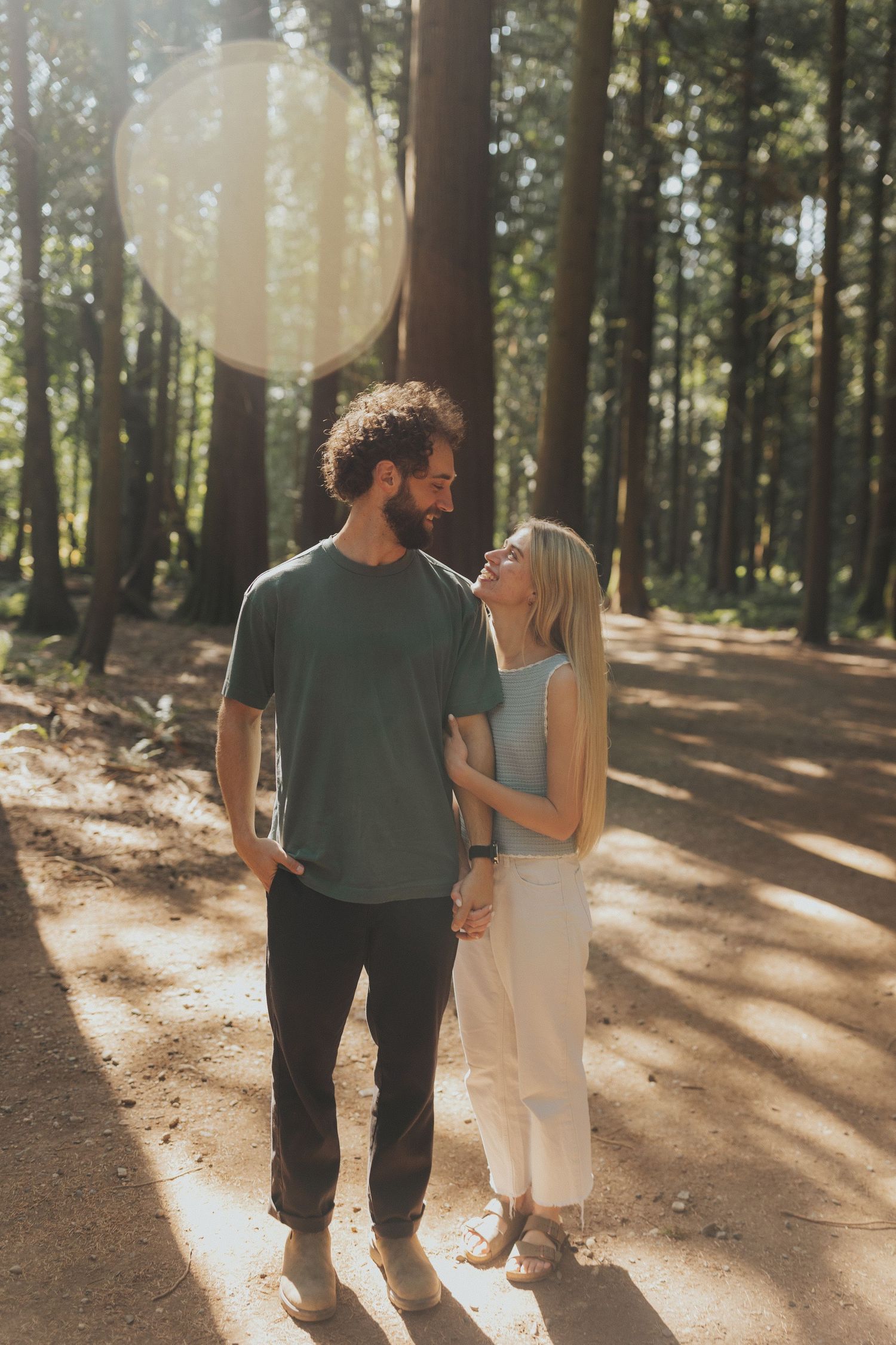 A couple walks intimately together through a sun-drenched forest path.