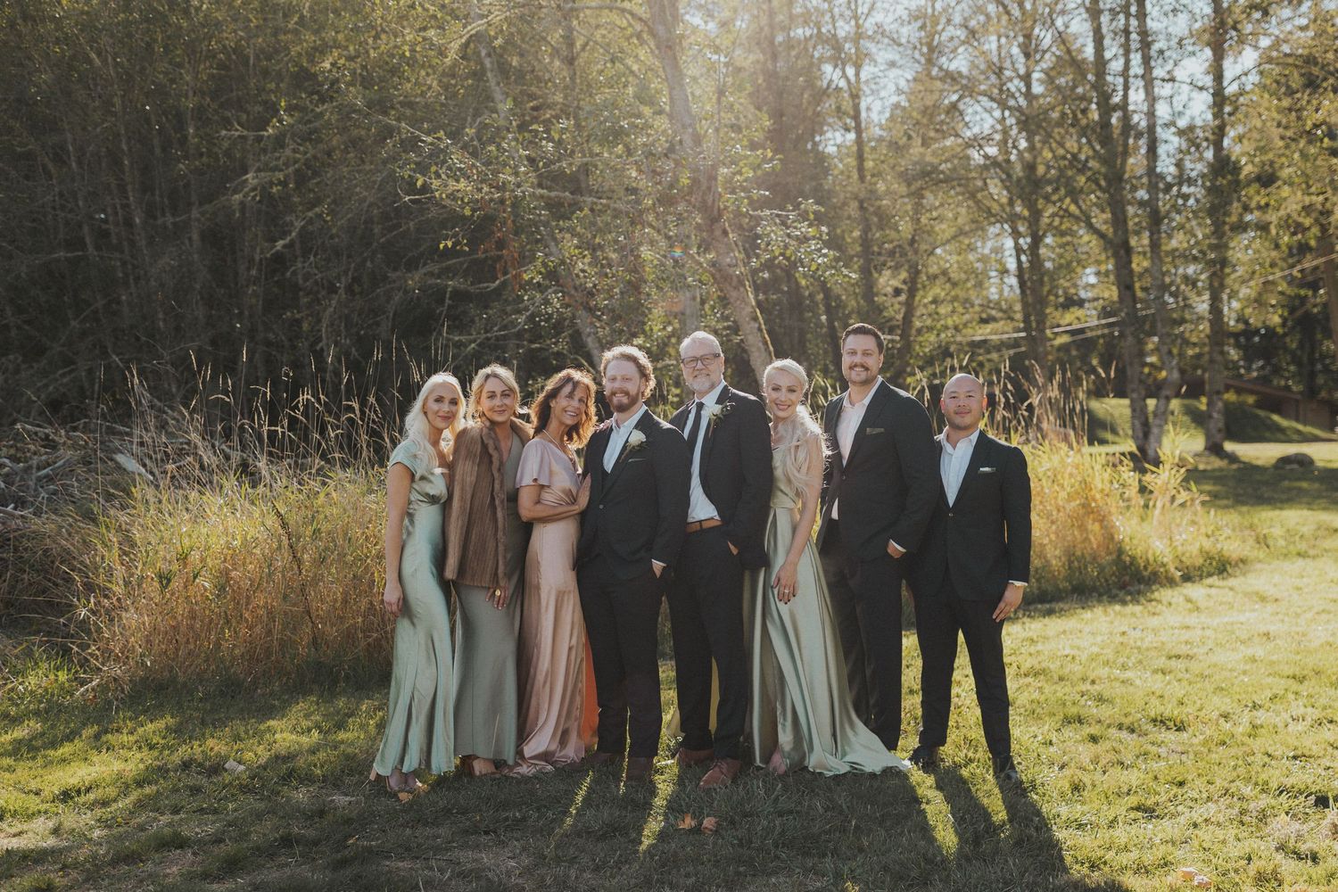 Wedding party in coordinated attire poses together in an outdoor autumn setting.